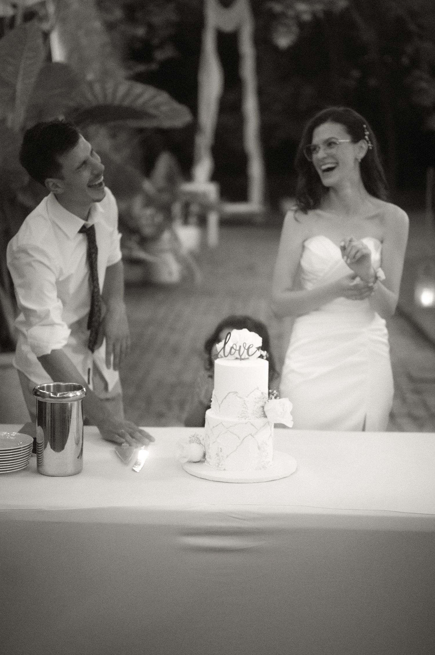 Black and white photo series showing a couple sharing cake and laughter at a wedding reception celebration.