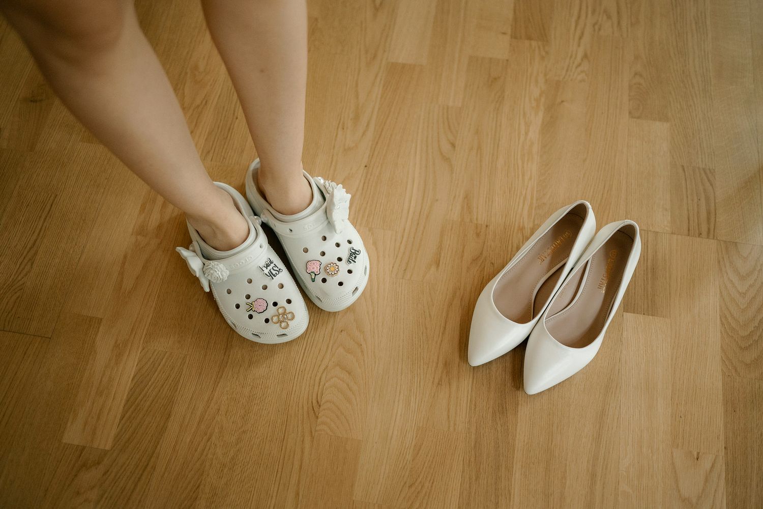 A collection of different white shoes and slippers arranged on a light wooden floor showing various footwear styles.
