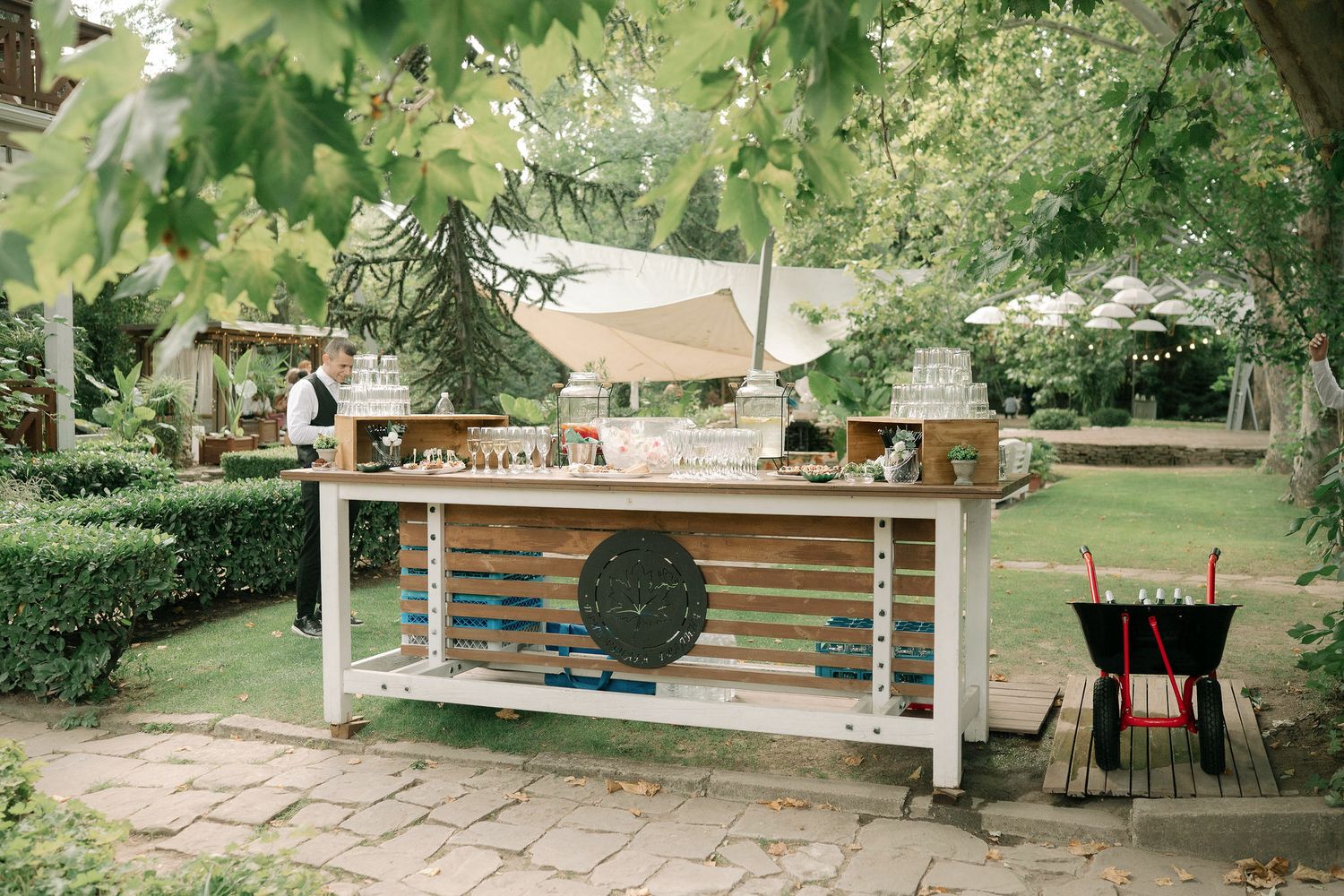 Rustic outdoor kitchen setup with wooden bar counter and grill in a lush garden setting.
