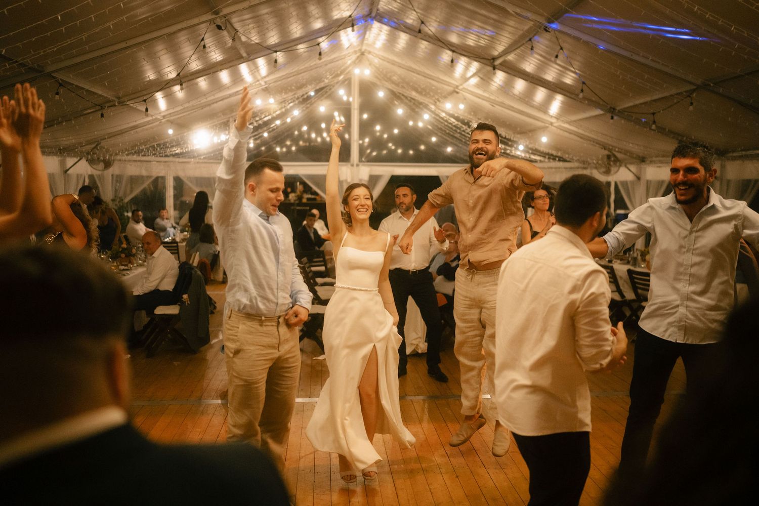Guests celebrating and dancing at a wedding reception under warm lighting in a barn-style venue.