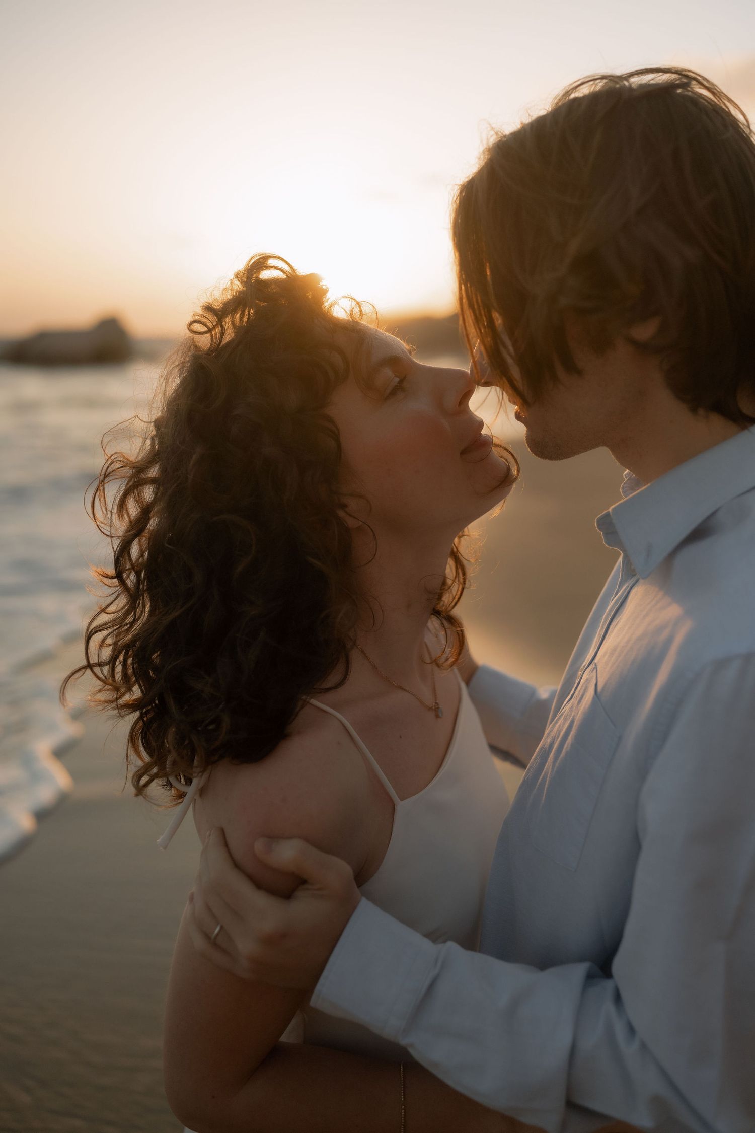 Romantic couple sharing a kiss on a beach at golden sunset, waves in background.