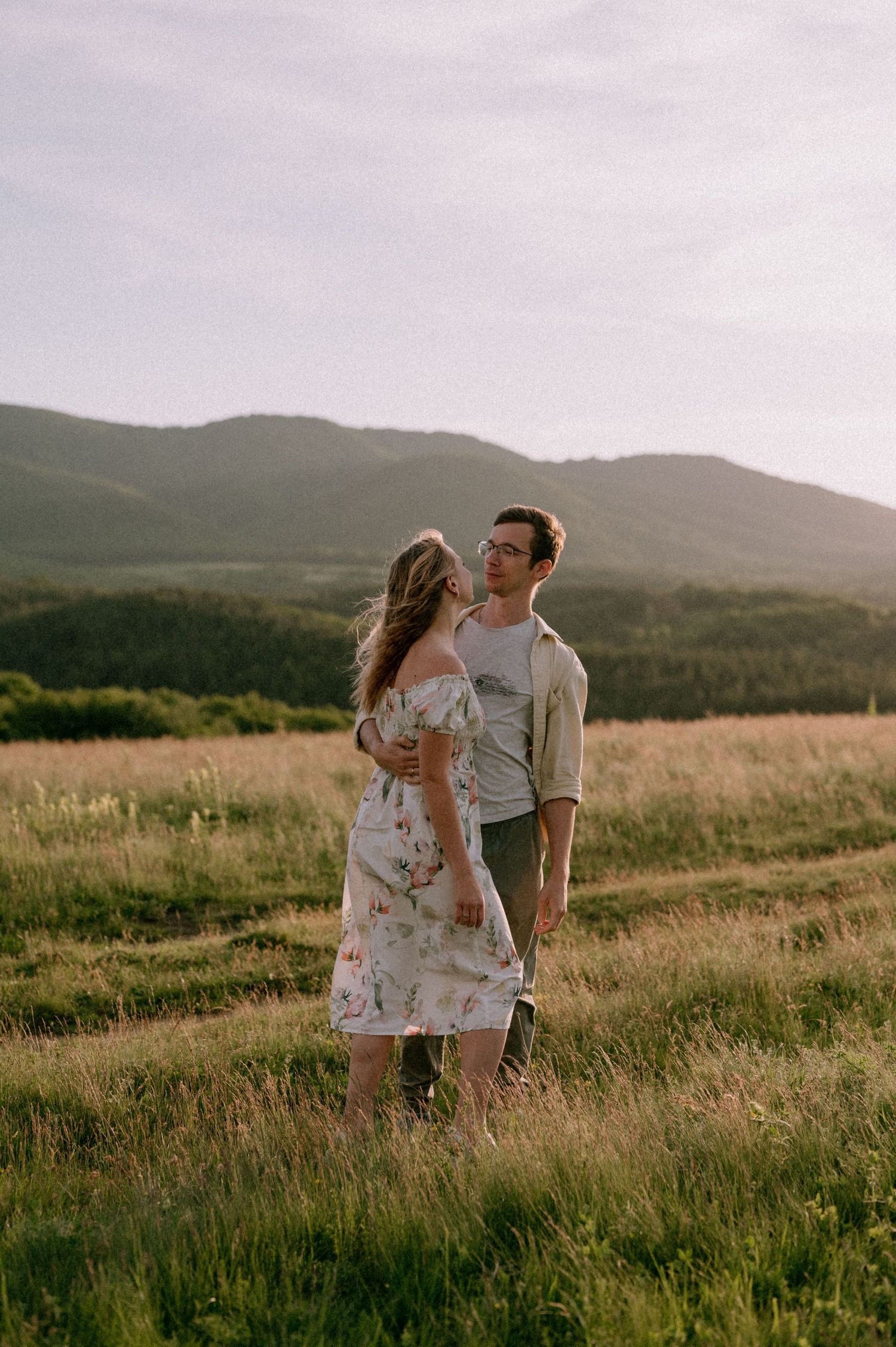 Couple sharing intimate moments in a scenic mountain field at sunset.