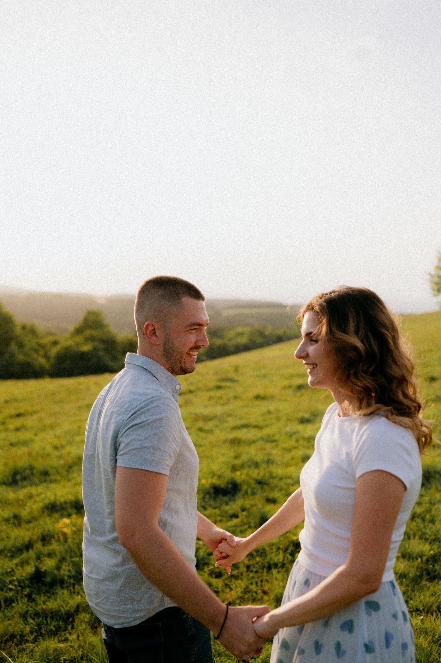 Couple sharing an intimate dance moment in a sunlit field with rolling hills behind them.