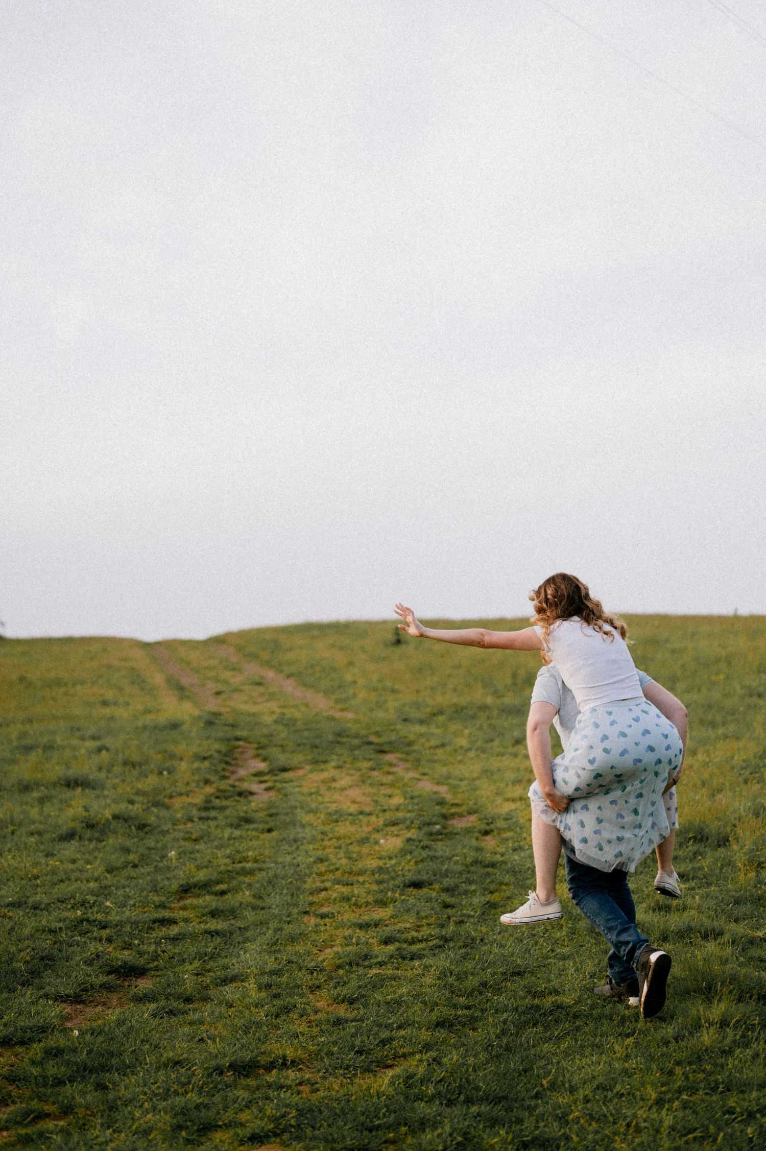 A person in a polka dot dress runs playfully across a green hillside.