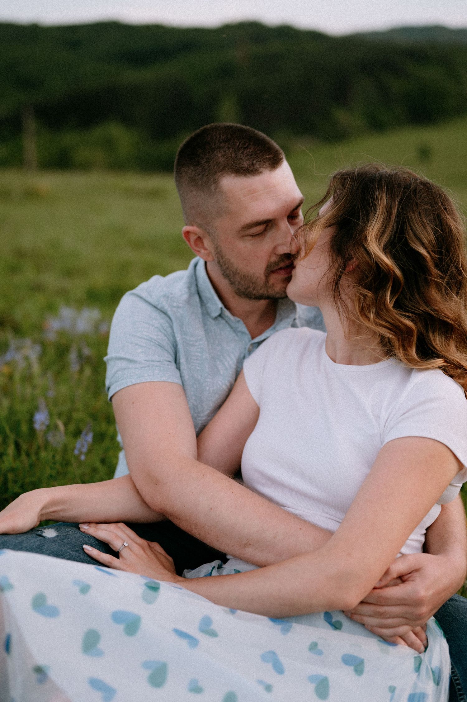Intimate portrait of couple embracing on heart-patterned blanket in mountain field.