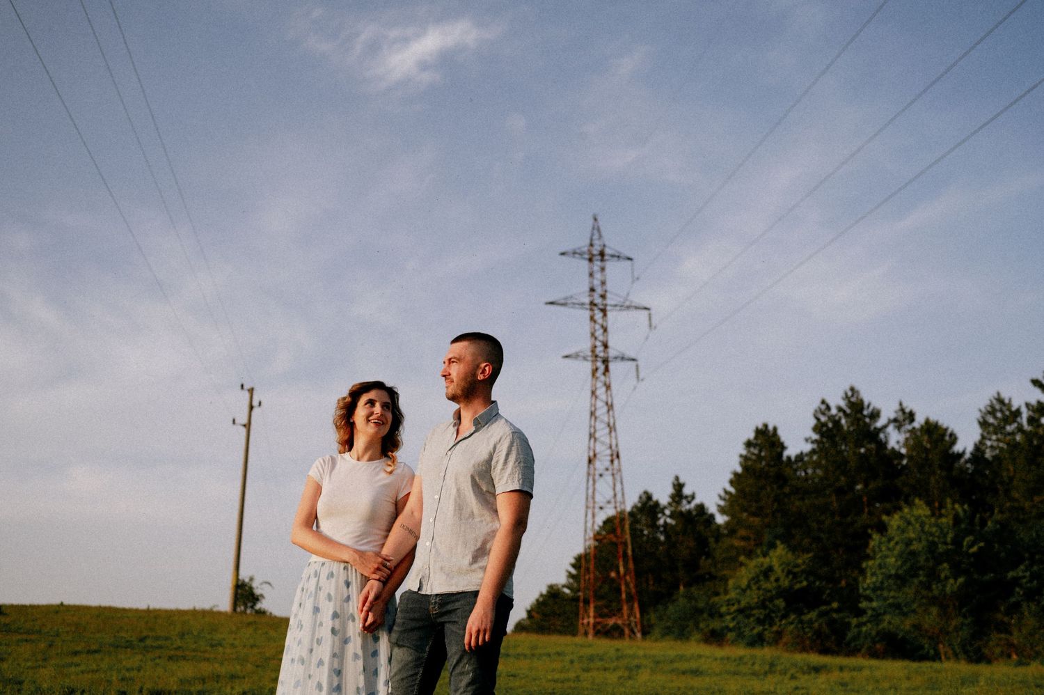 Couple standing beneath power lines in a rural setting at dusk.