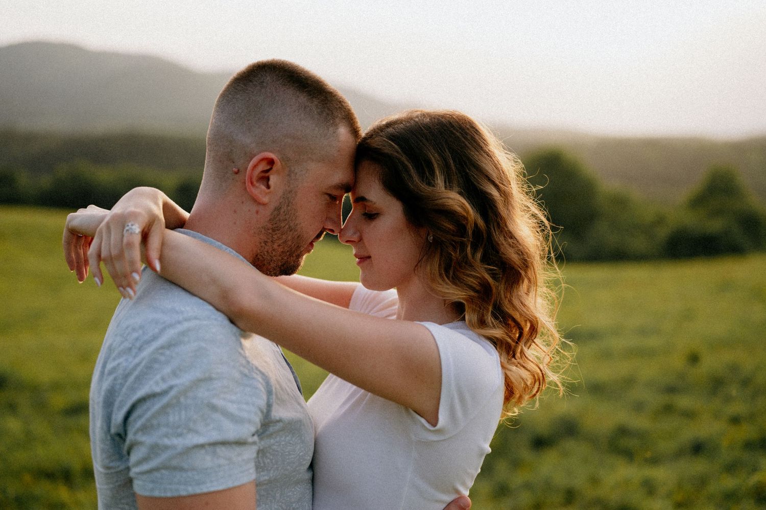Romantic couple embraces in a sunlit meadow during golden hour photography session.
