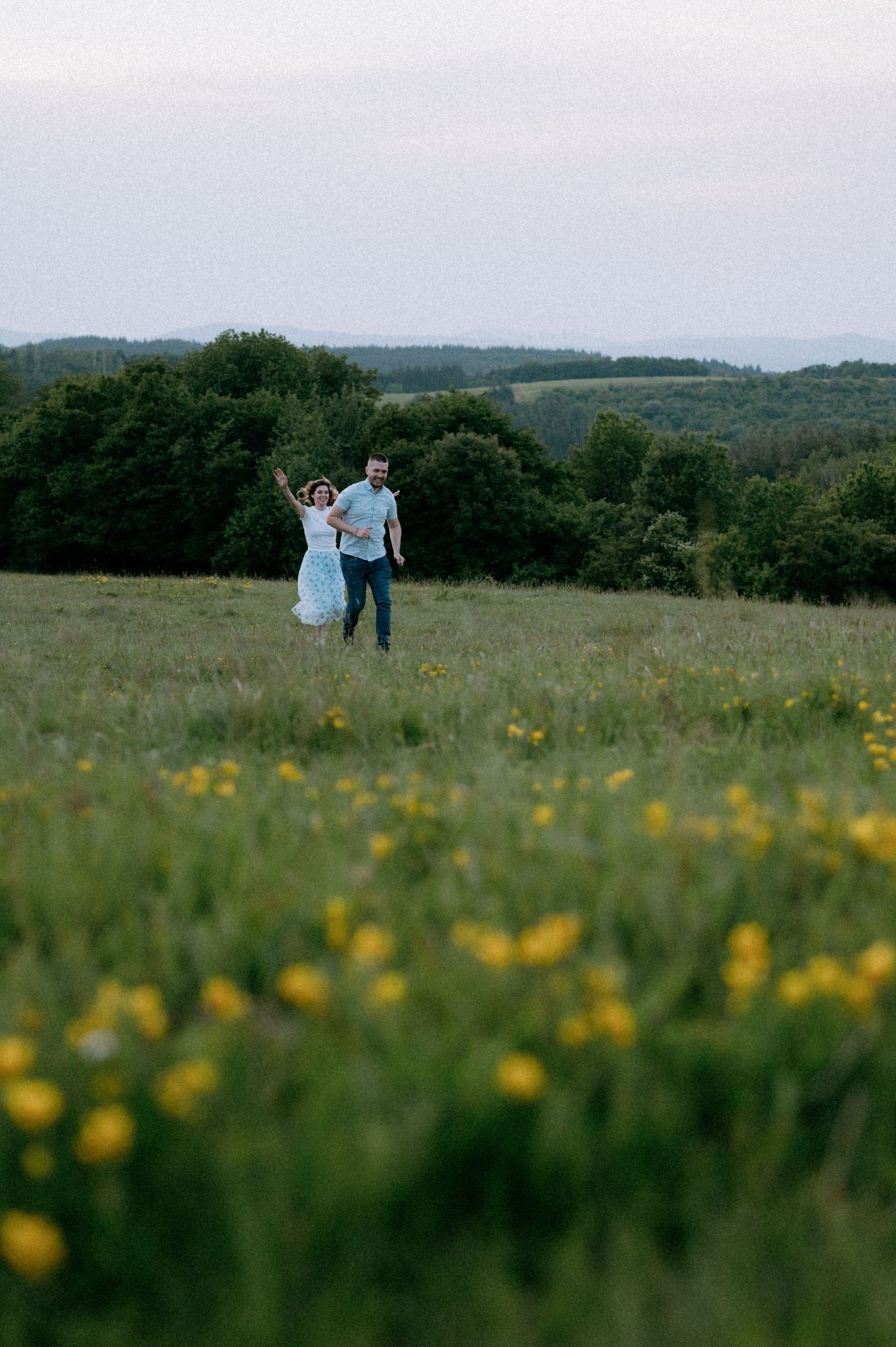 A couple dances playfully in a meadow filled with yellow wildflowers during golden hour.