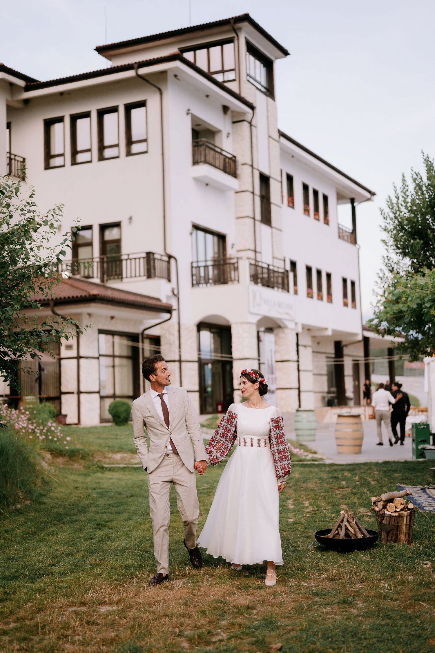 Couple celebrating at an outdoor wedding near a white villa with bonfire setup.