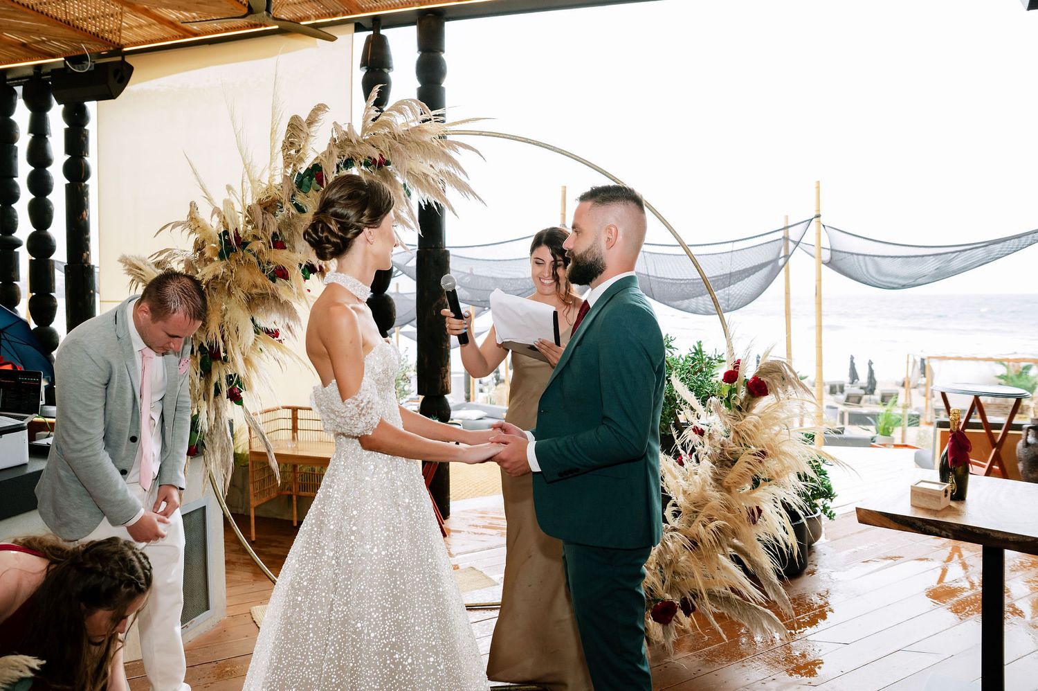 Wedding ceremony in an industrial-style venue with hanging lanterns and pampas grass arrangements.