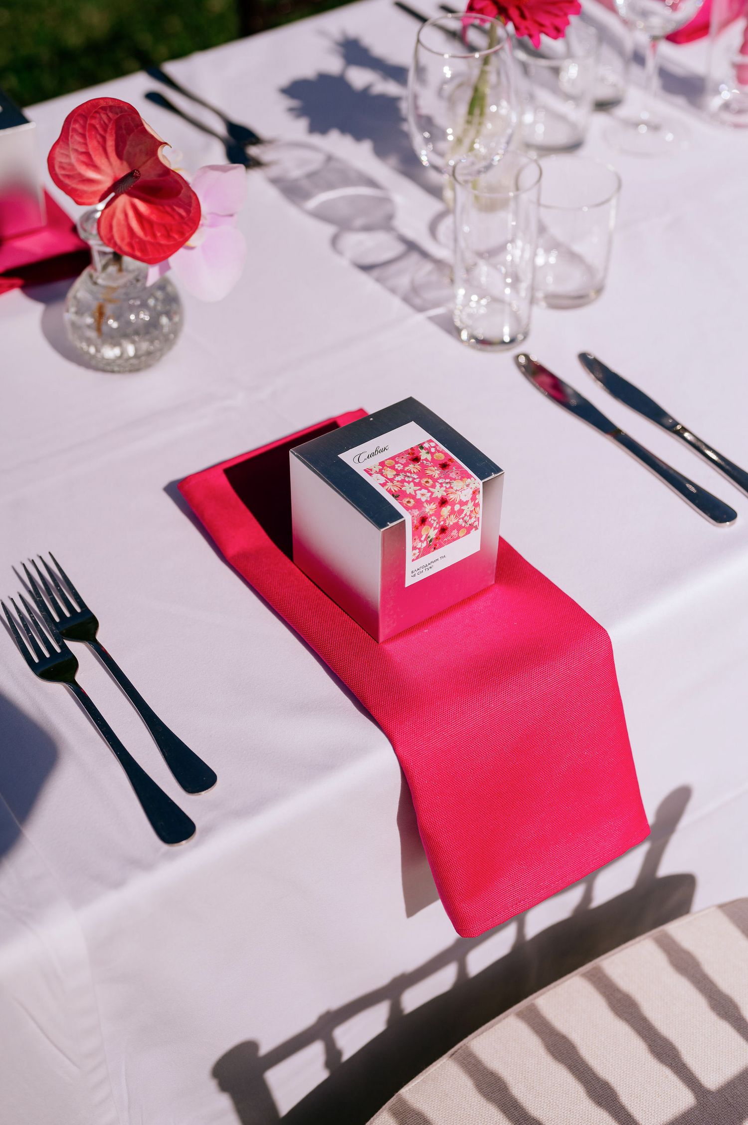 Close-up of formal table setting with hot pink napkin, red flowers, and crystal glassware.