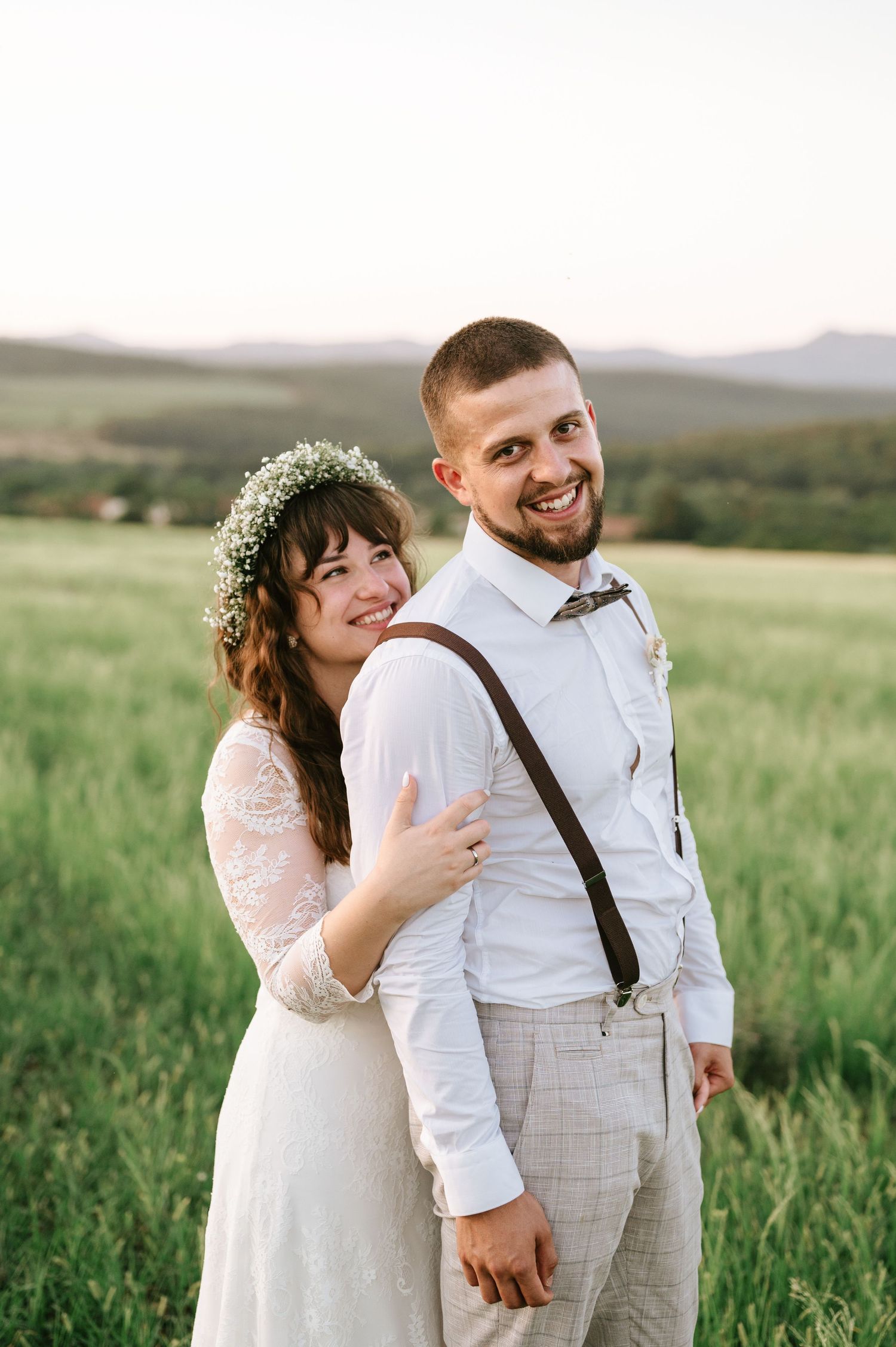 A romantic outdoor wedding portrait in a grassy field at sunset.