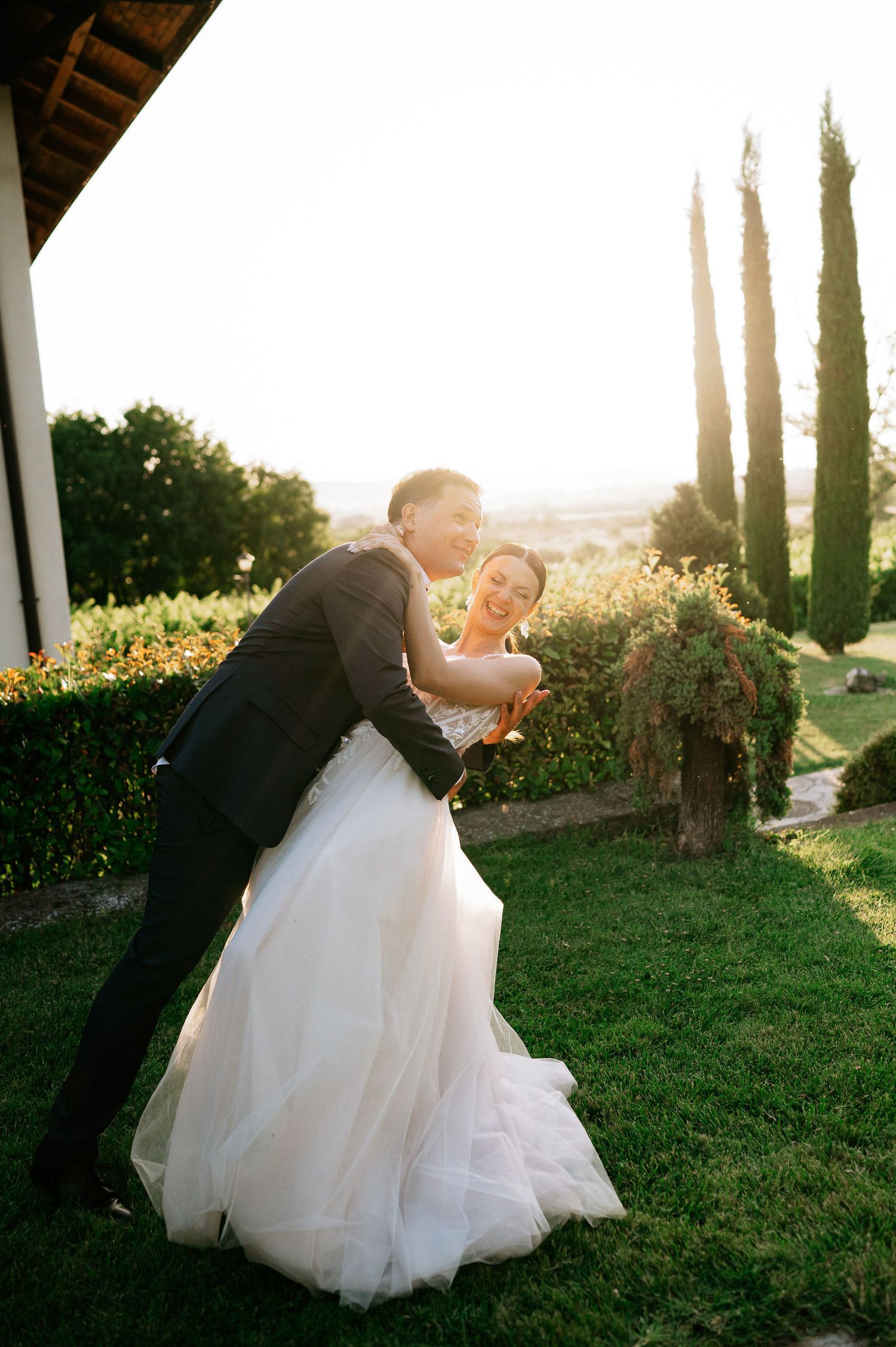 Couple shares romantic dip pose against scenic garden backdrop at sunset.