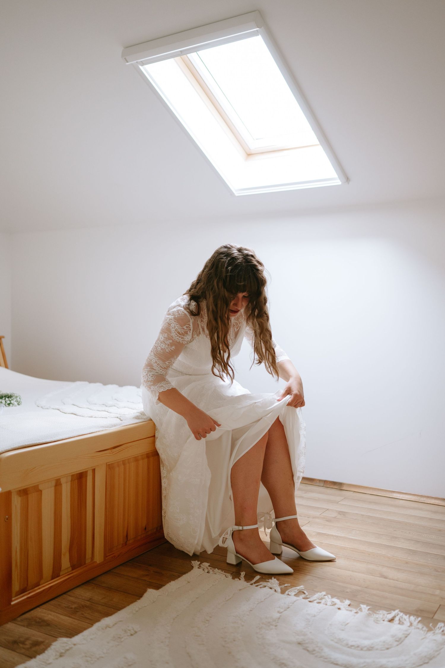 Person in a white wedding dress sitting on wooden floor in an attic room.