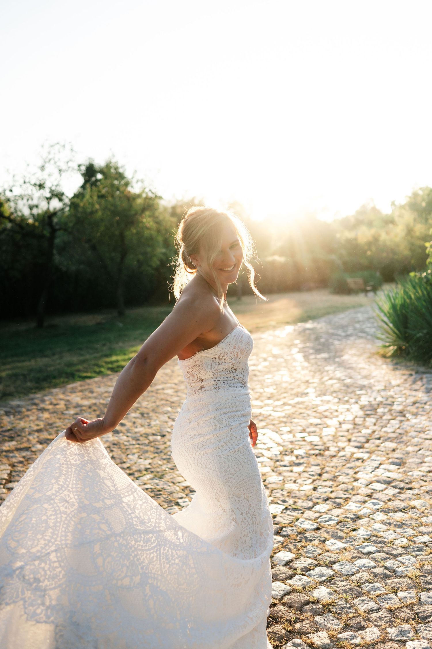 Sunlit bridal portrait showing graceful movement of lace dress against natural backdrop.