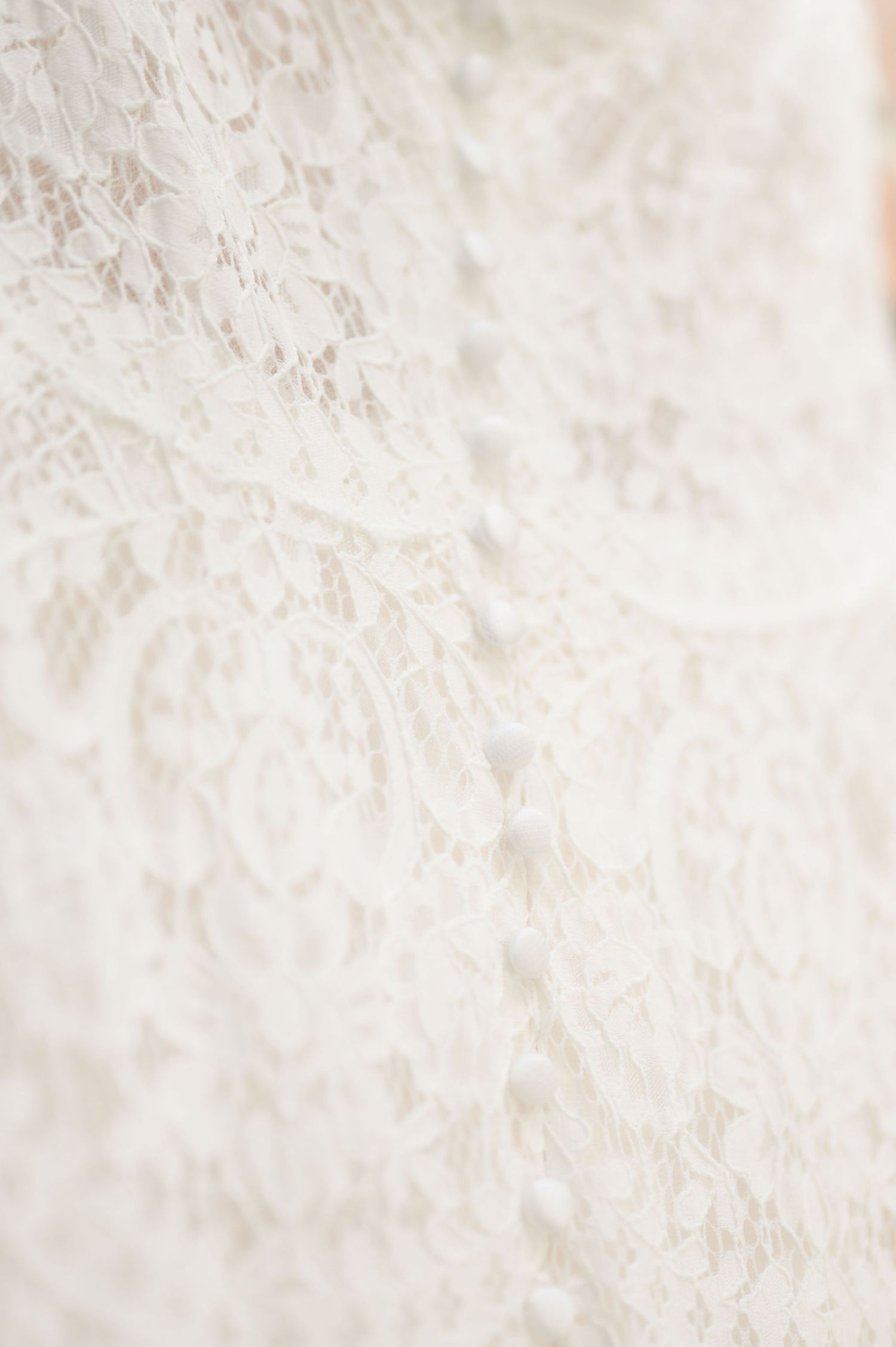 Close-up detail of delicate white lace wedding dress fabric texture.