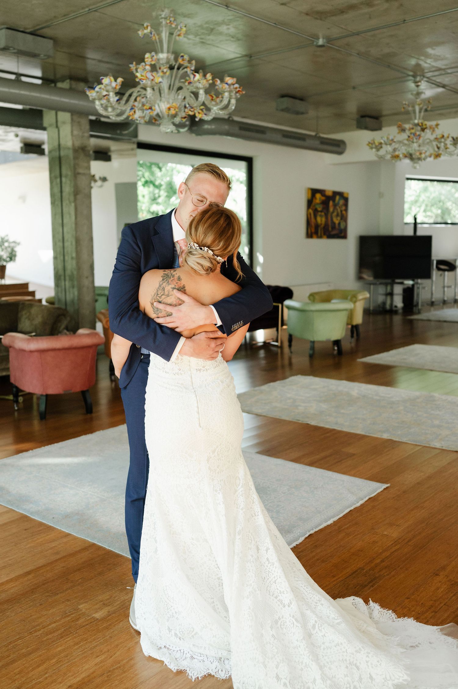 Newlyweds share a romantic dance moment on a wooden floor under crystal chandeliers.