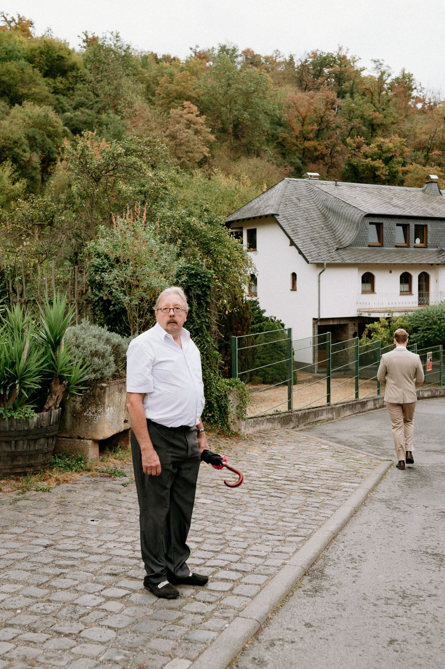 A cobblestone path leads to a white house nestled among trees on a hillside.