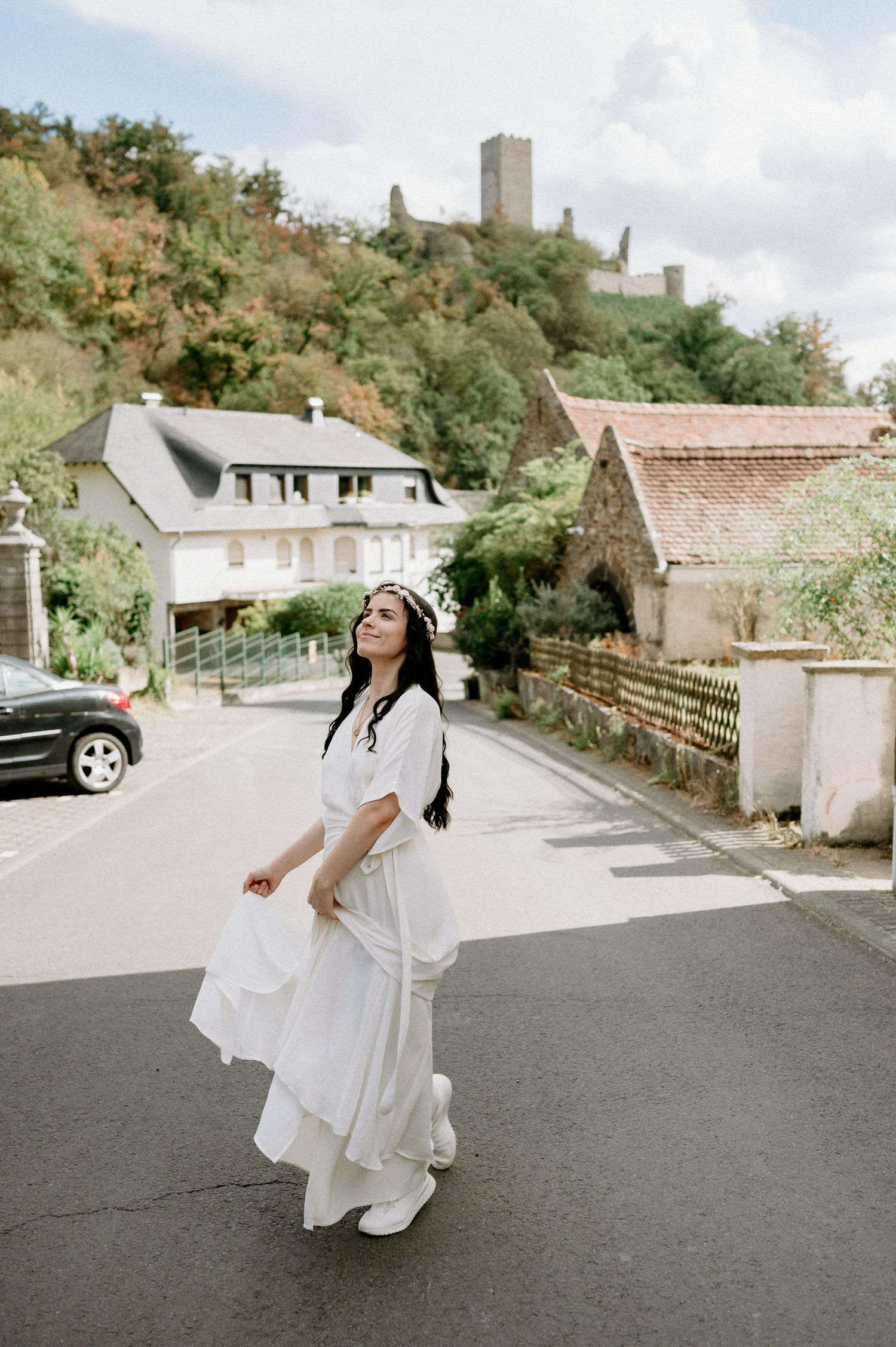 Bride in flowing white dress twirling on a quiet street with buildings in background.