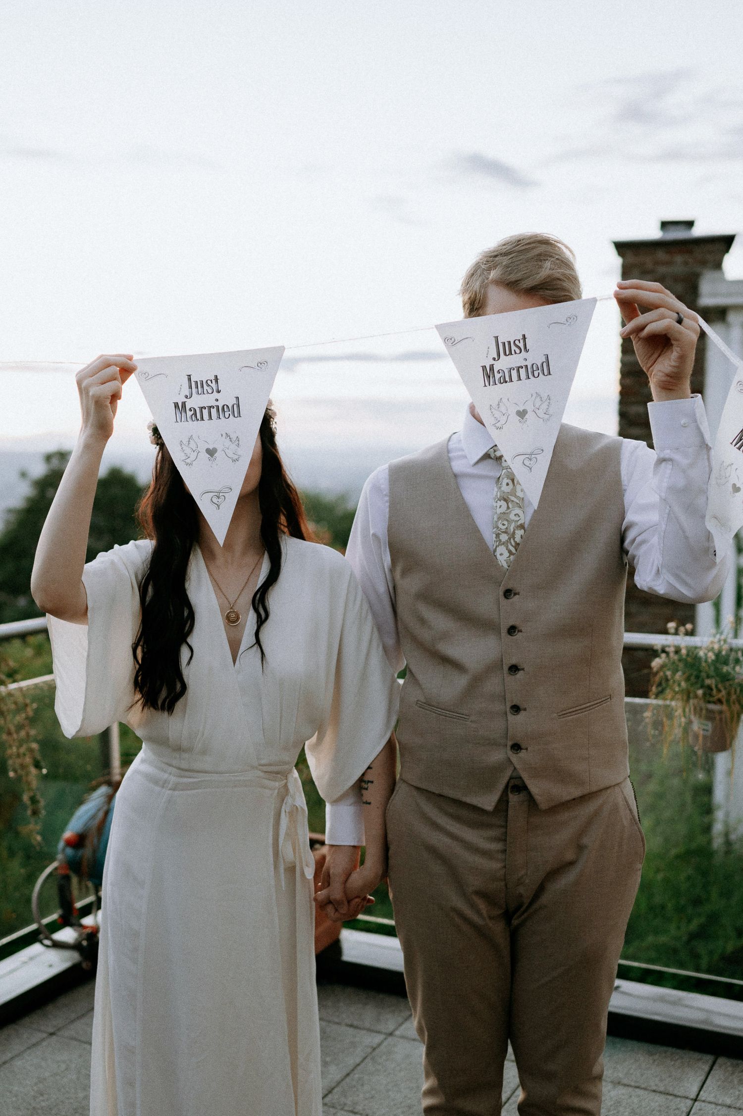 Couple holding 'Just Married' banner triangles on an outdoor balcony.