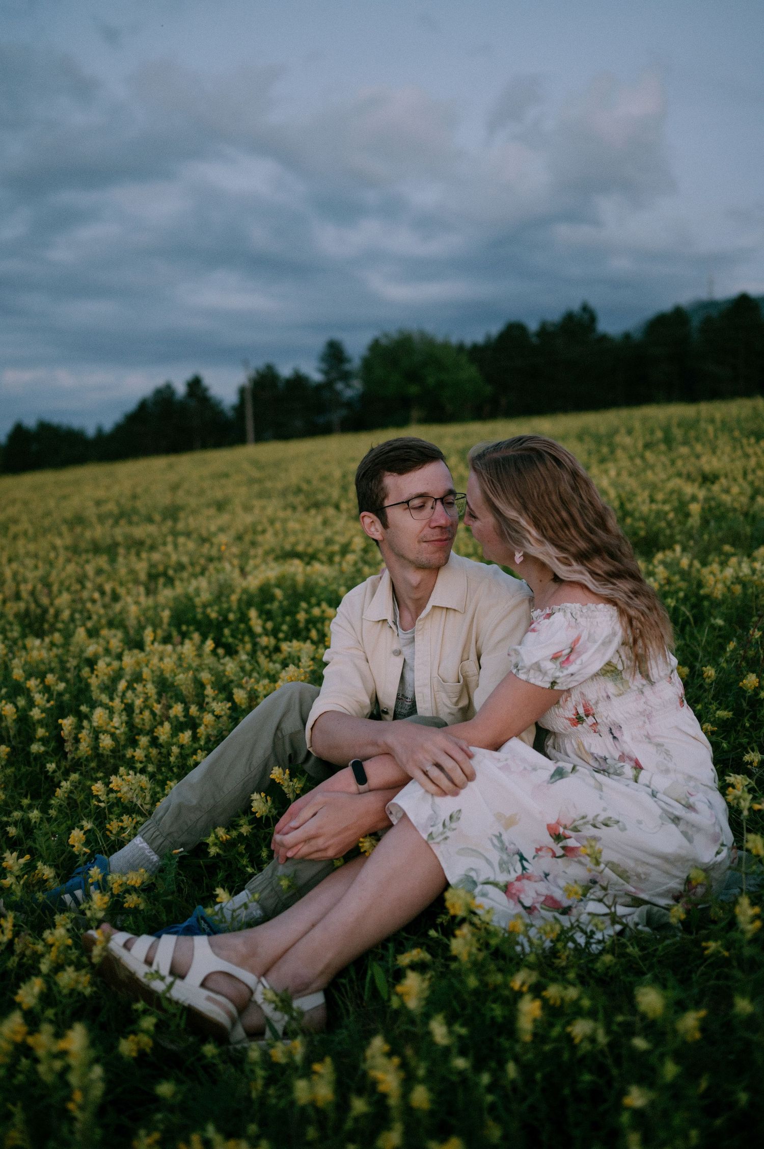 Two people share tender moments while relaxing in a blooming canola field at dusk.