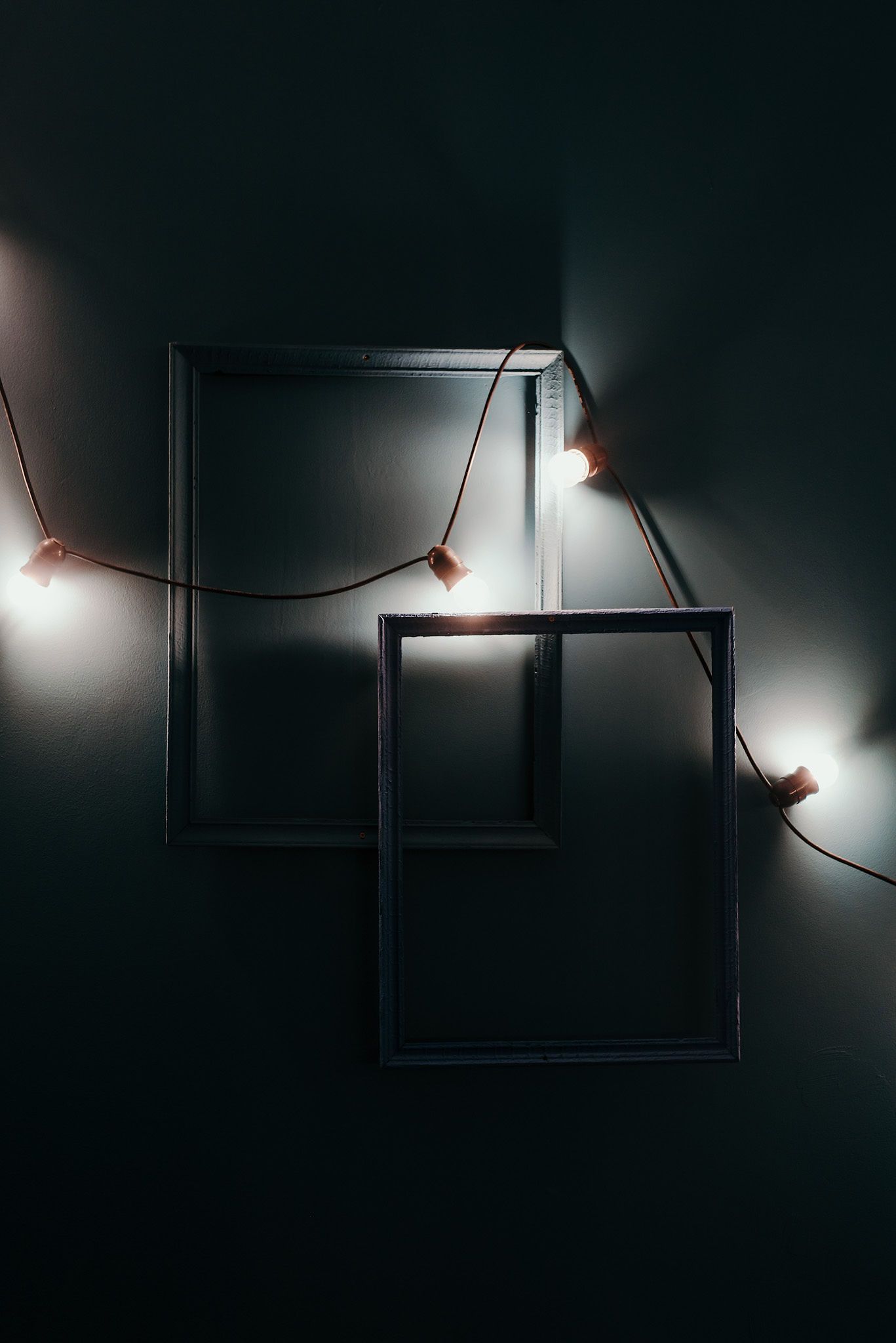 Minimalist empty picture frames on dark wall with string lights creating geometric shapes.