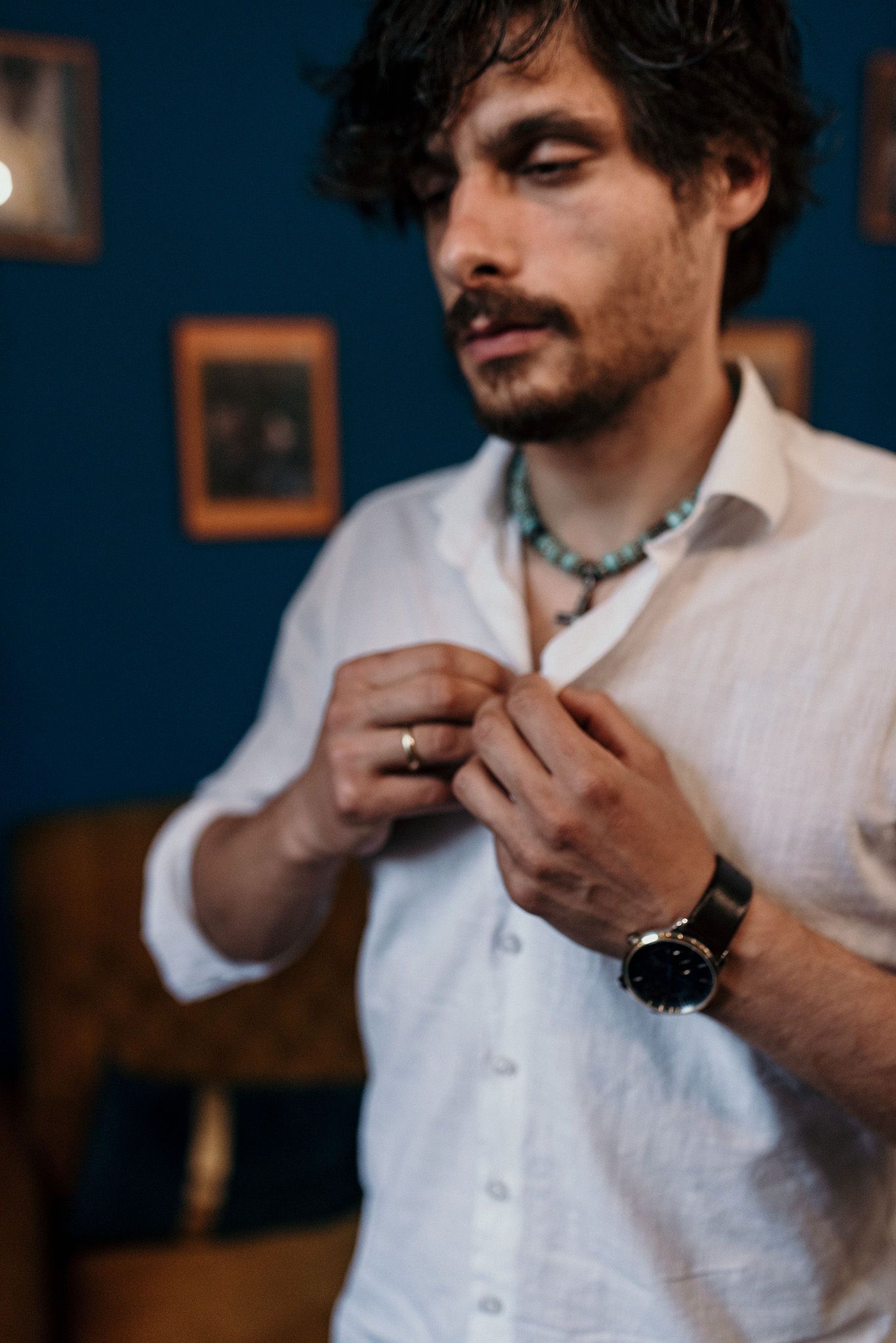 Person in white button-down shirt adjusting collar against deep blue wall.