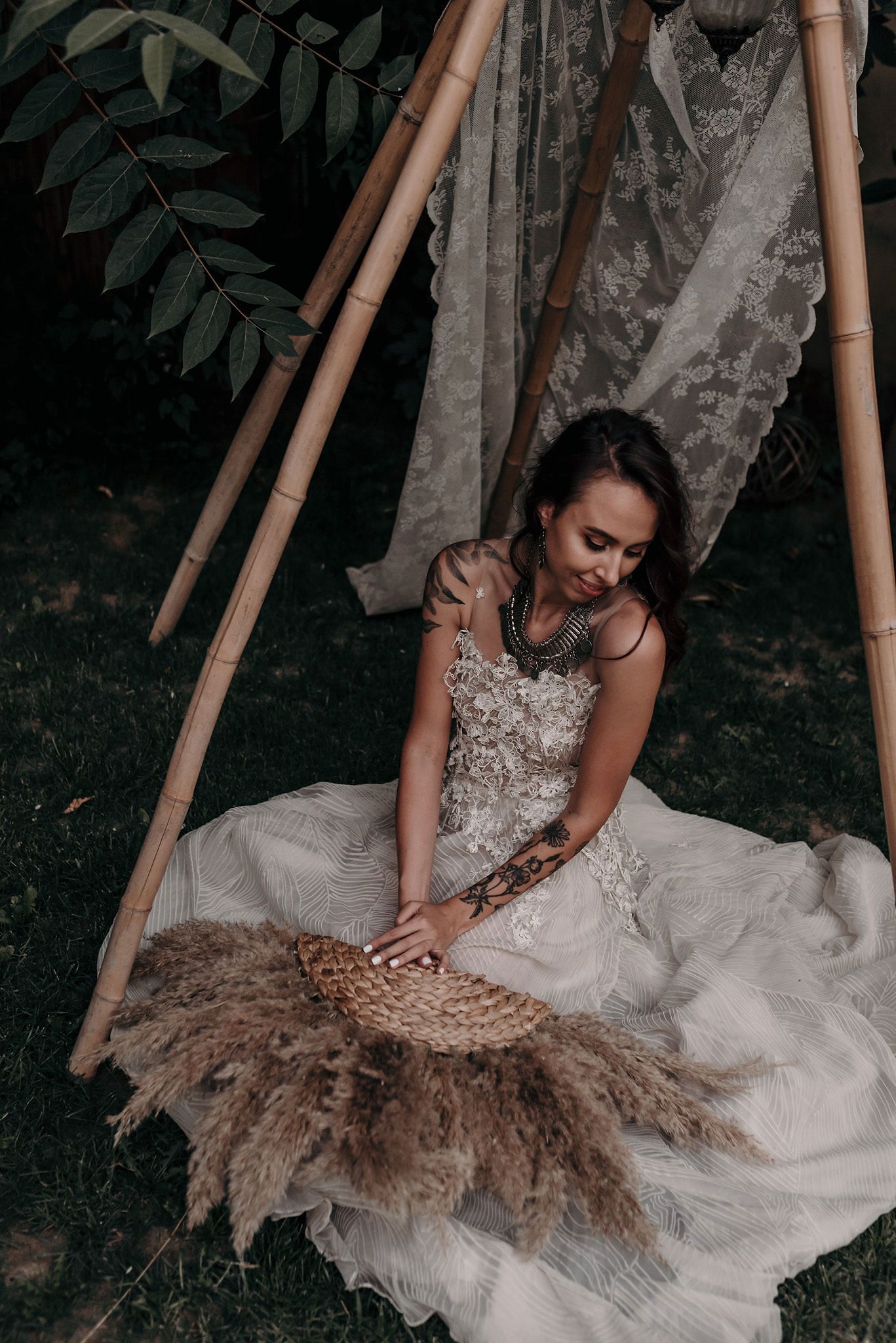 A person in an elegant white wedding dress with intricate lace details sits gracefully on the ground.