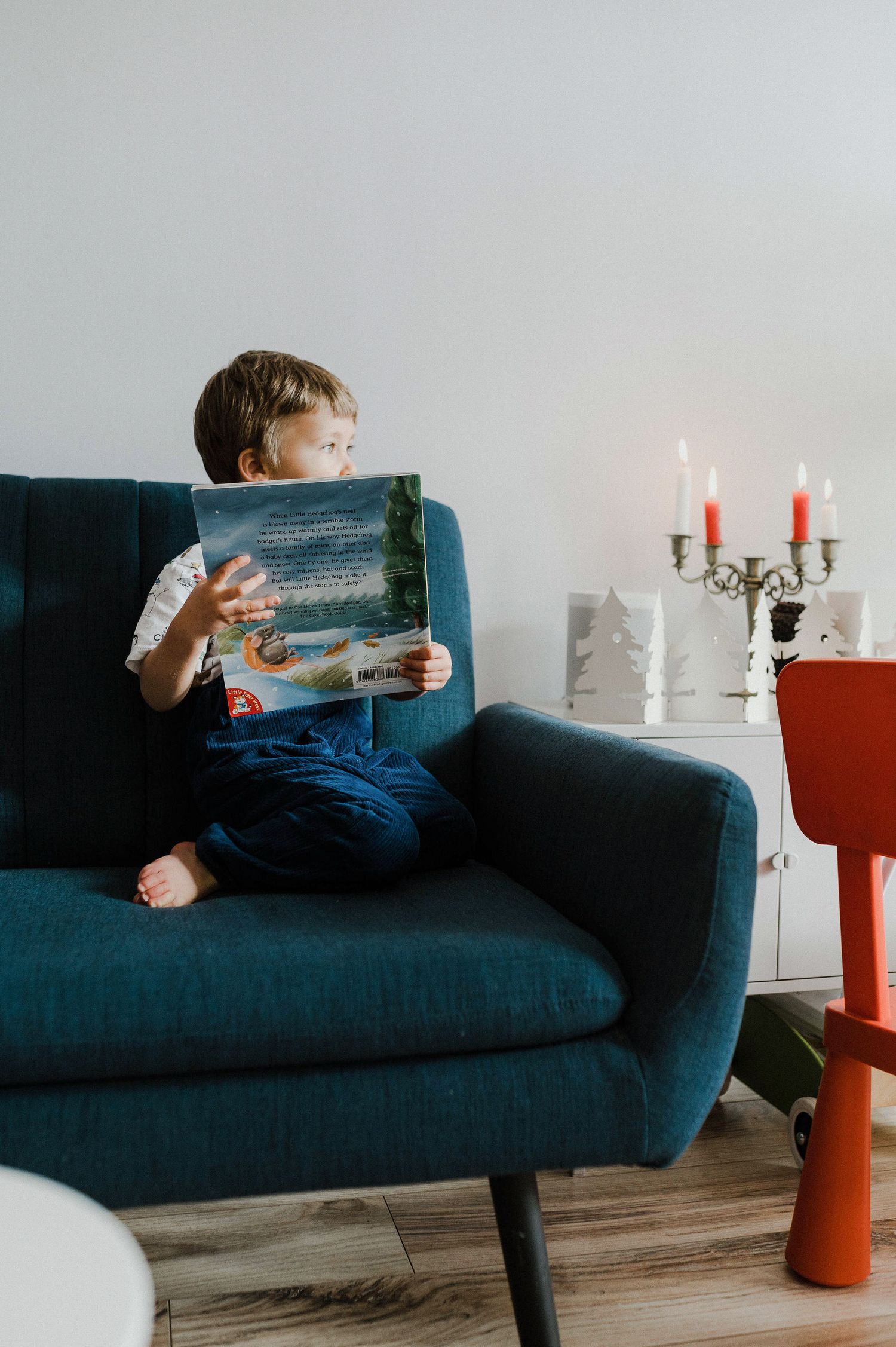 Someone reads a book while relaxing on a navy blue couch with red candles and white decor visible in the background.