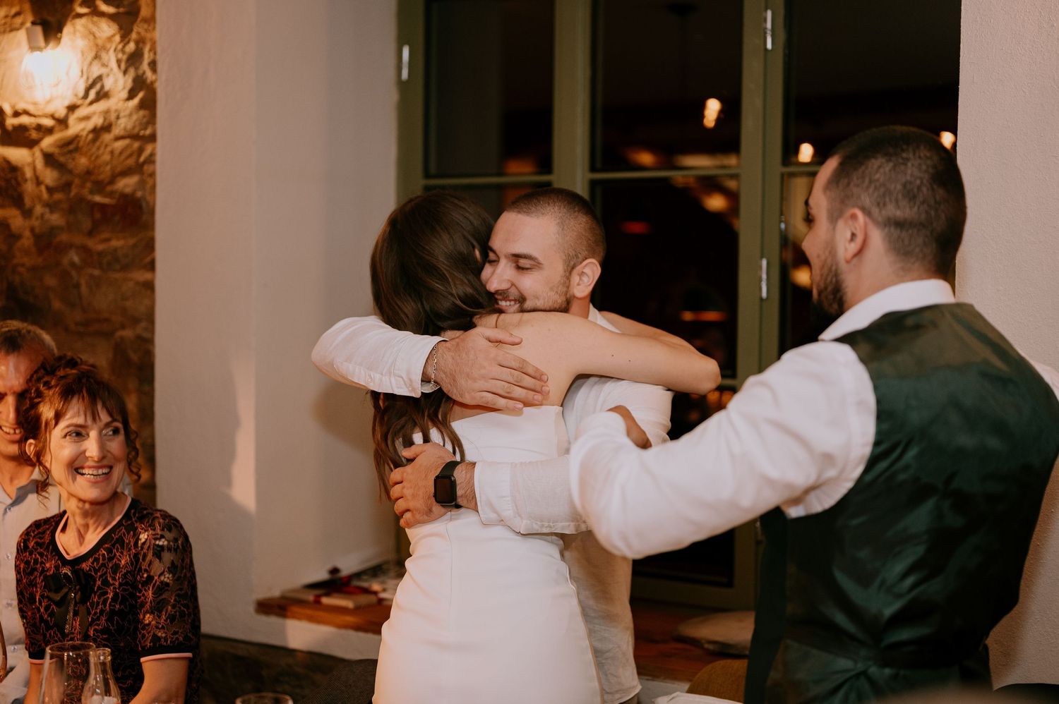 Wedding celebration showing guests embracing and toasting at a rustic venue with stone walls.