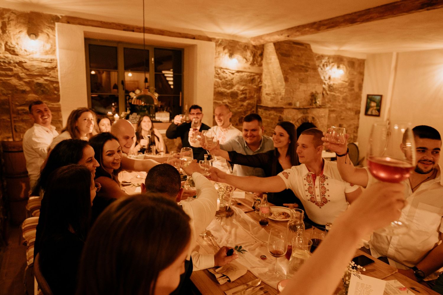 Guests raising glasses for a toast at a long dining table in a rustic room.