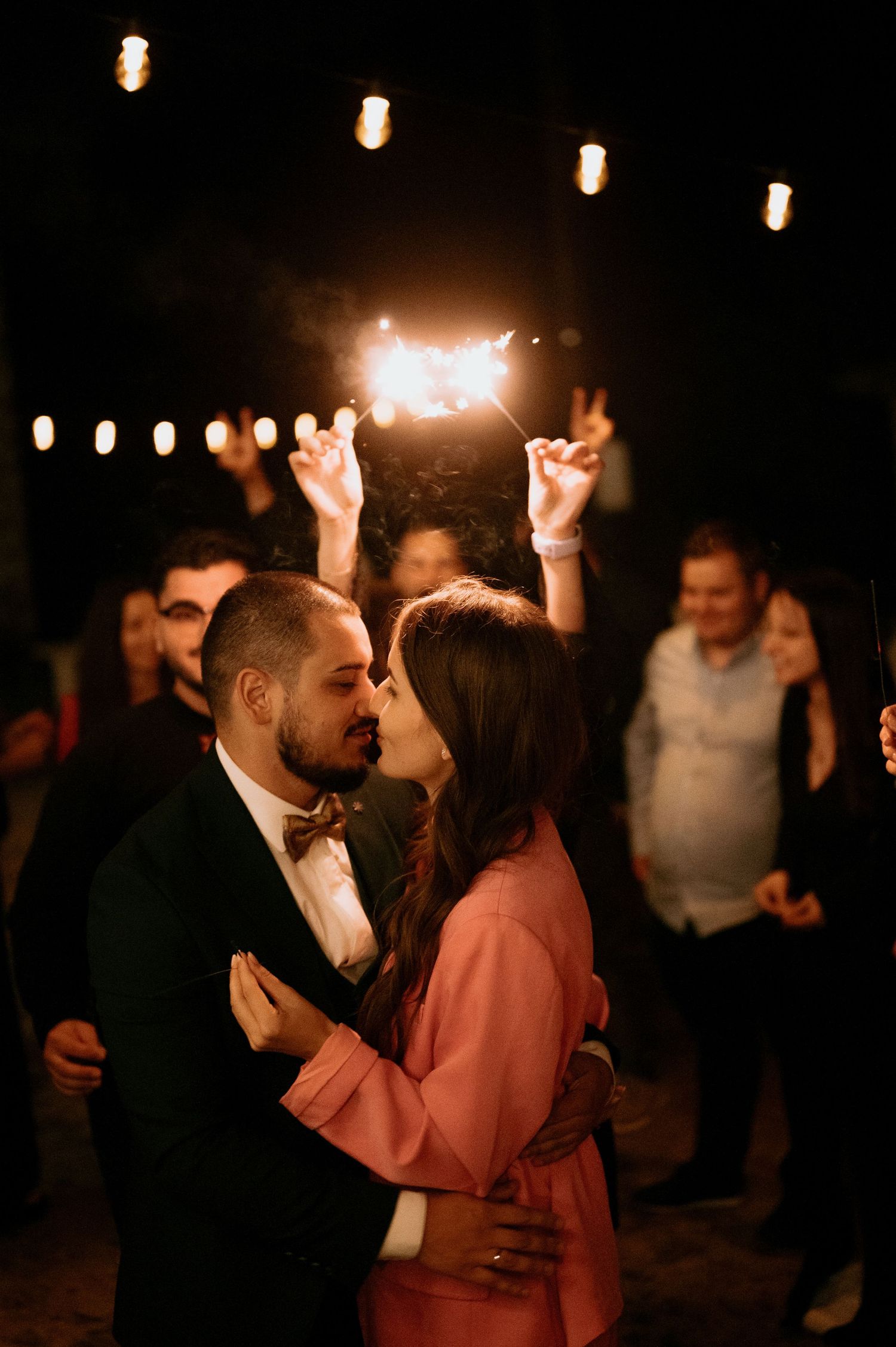 Couples dancing under string lights at outdoor nighttime celebration.