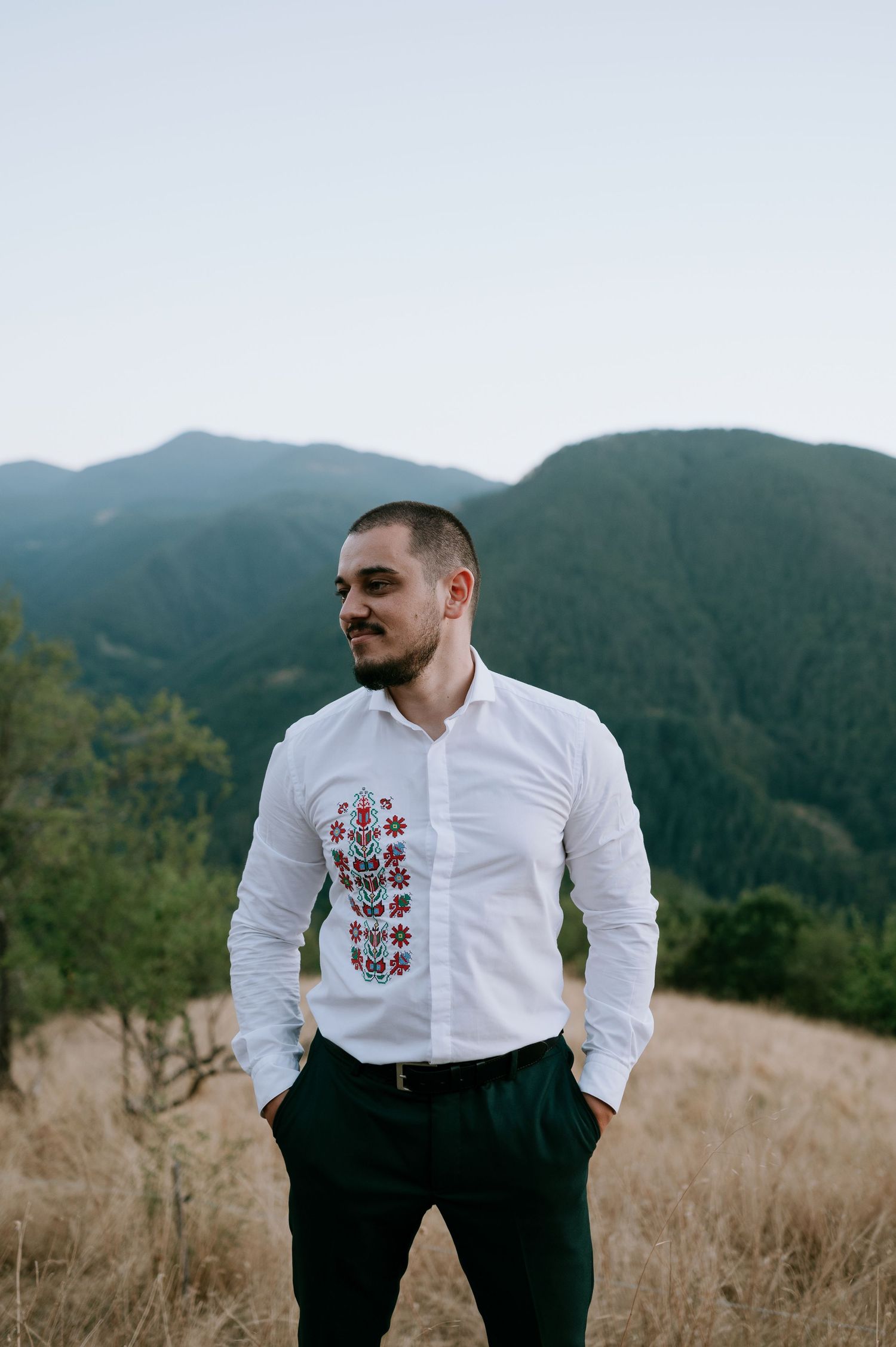 Wedding attire featuring embroidered white shirt against mountain landscape backdrop.