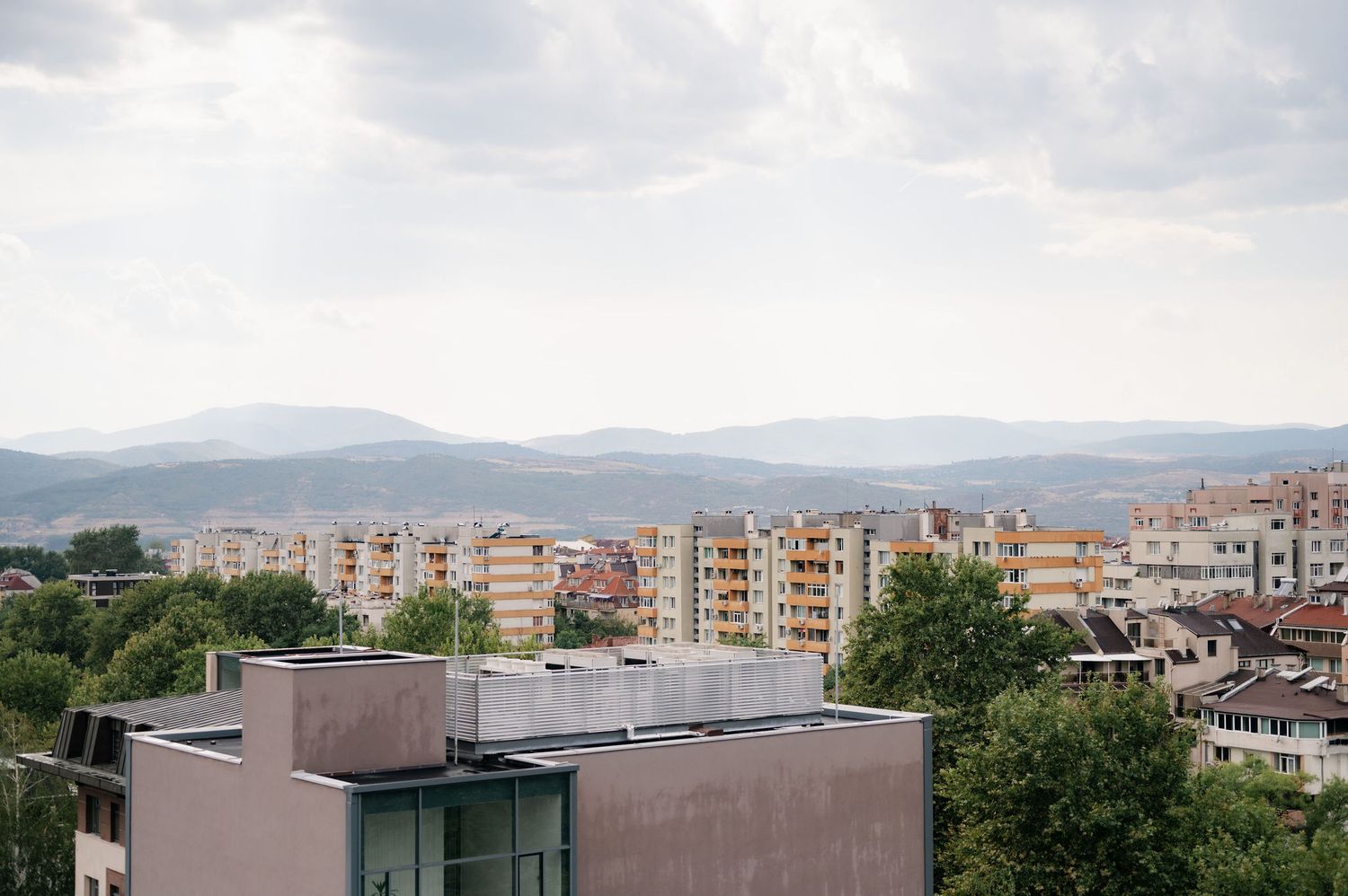 Panoramic cityscape view of residential buildings and mountains in the distance under cloudy skies.