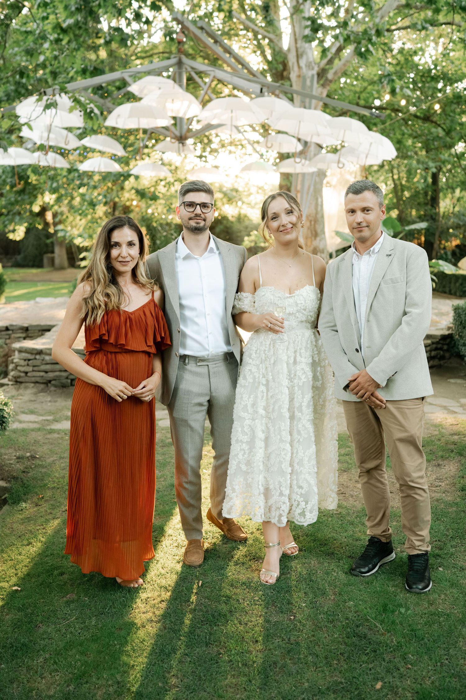 Wedding group photo with attendants in burgundy and gray outfits posing casually on grass.