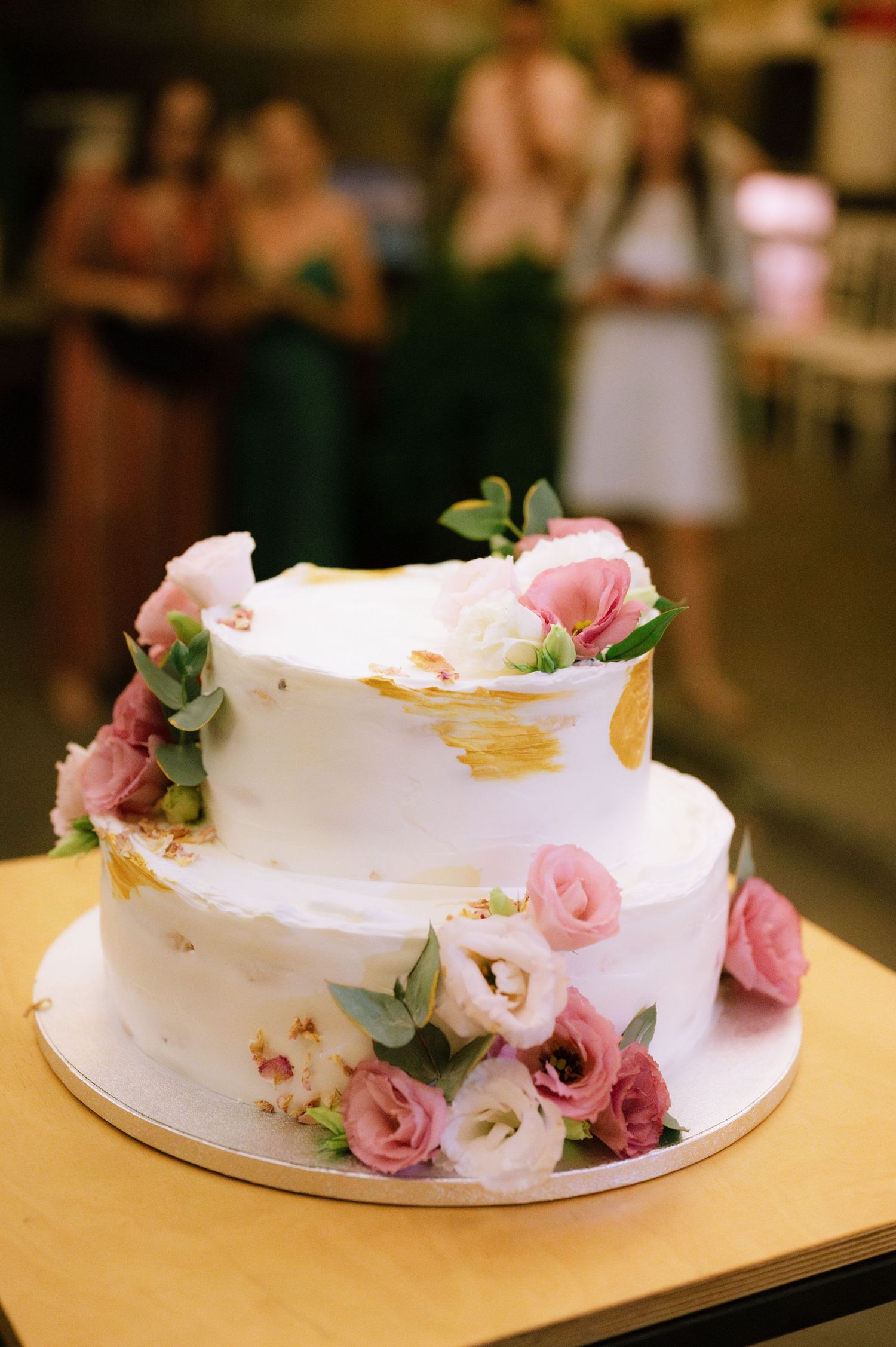 A white wedding cake decorated with delicate pink roses and eucalyptus leaves sits on a wooden surface.