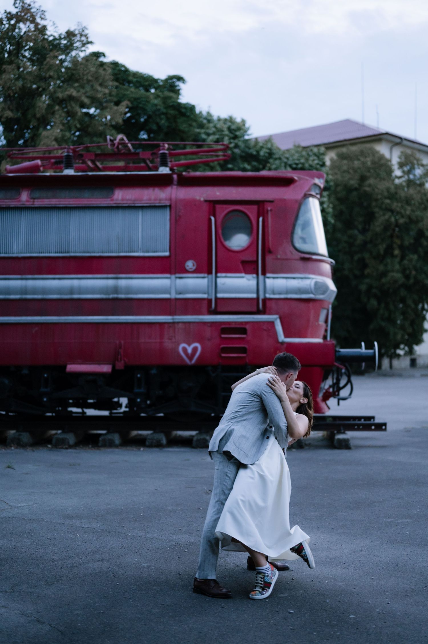 A series of romantic photos showing a couple embracing in front of a vintage red train at dusk.