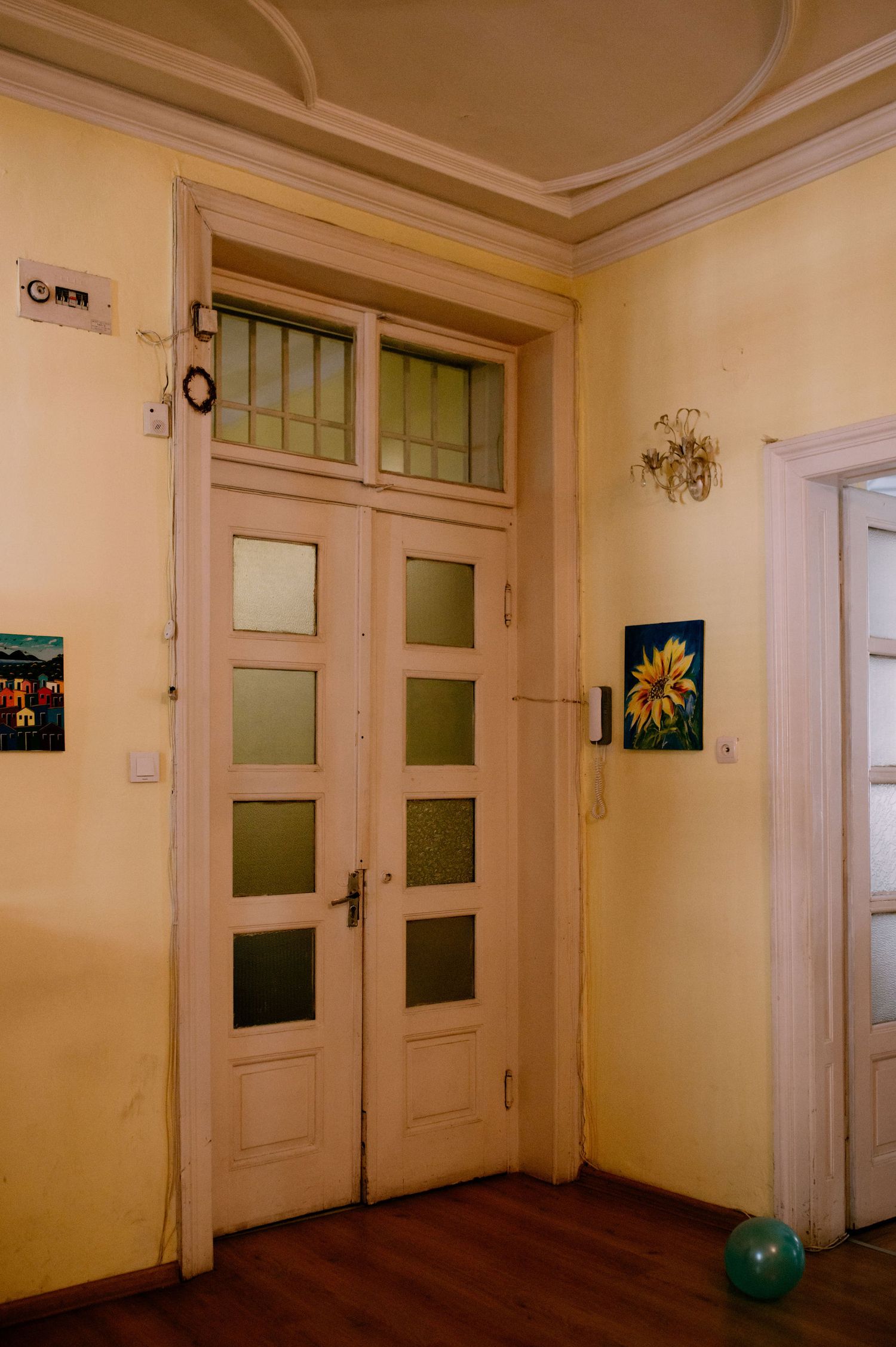 Vintage interior hallway with tall frosted glass double doors, cream walls, and a sunflower painting on display.
