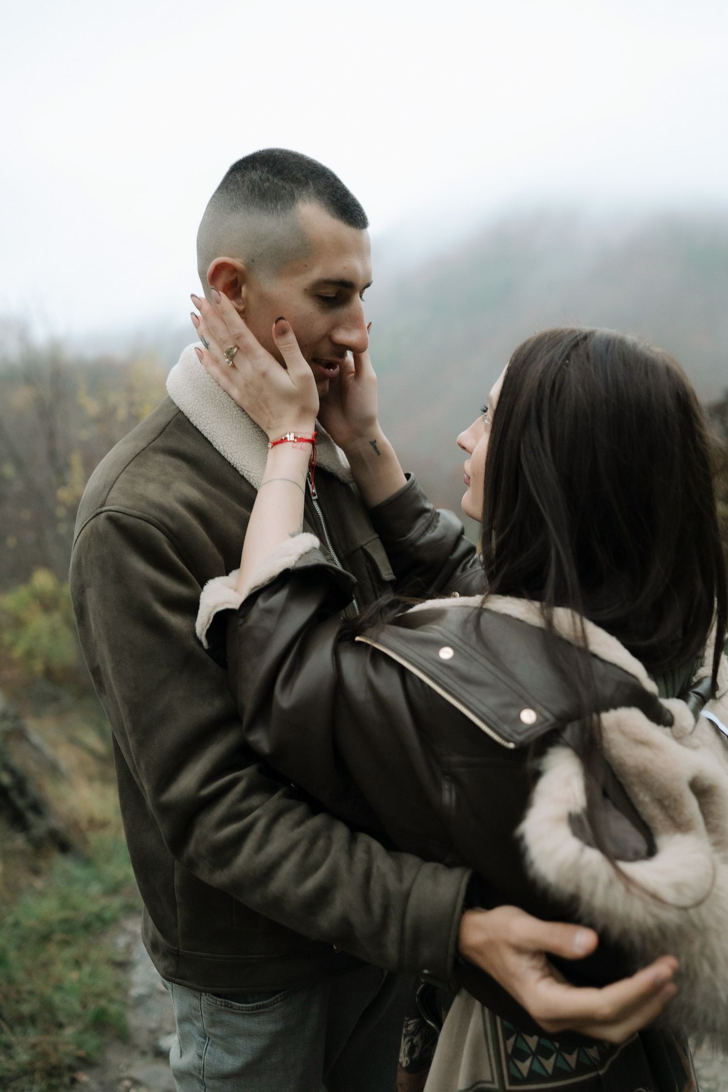 A romantic couple embraces while standing in a foggy outdoor setting during fall.