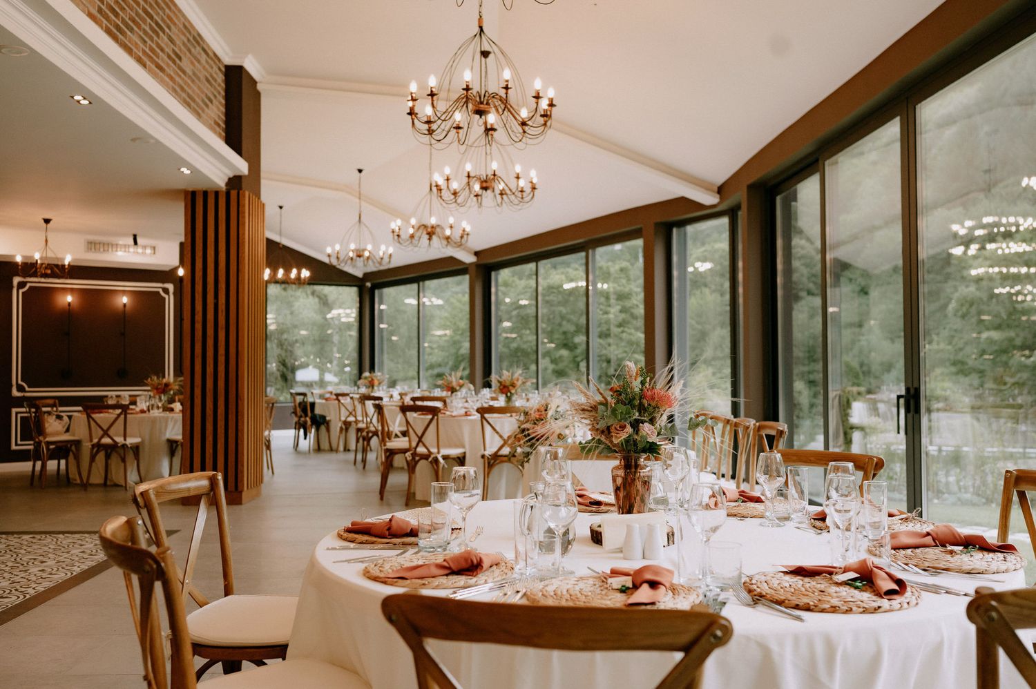 Elegant wedding reception venue with crystal chandeliers, floor-to-ceiling windows, and tables set for a formal dinner.