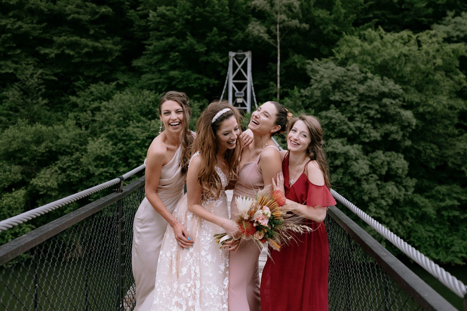 A group in formal attire shares a joyful moment on a suspension bridge surrounded by lush green forest.