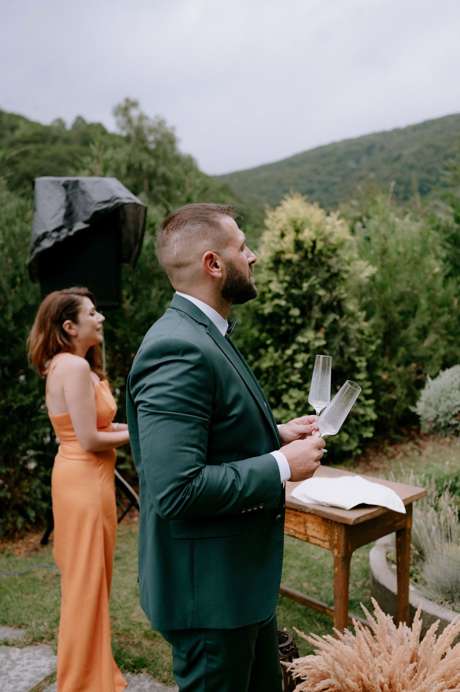 A couple reads letters to each other during an outdoor wedding ceremony surrounded by mountains and pampas grass.