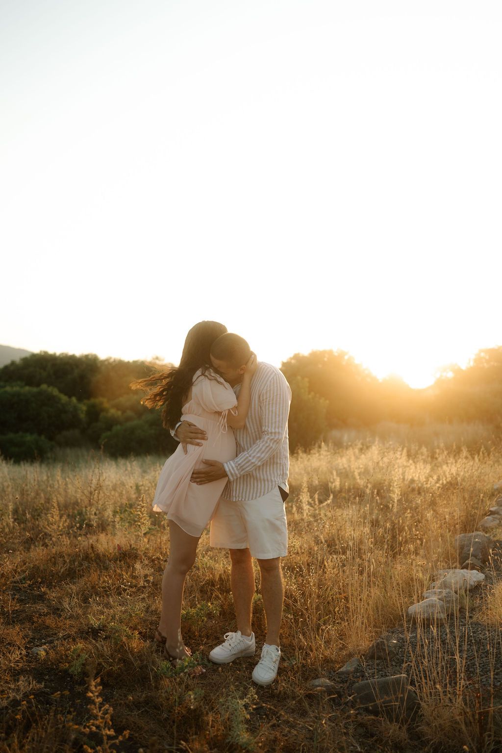 A couple embraces in a golden sunlit field at sunset creating a romantic silhouette against the warm evening sky.
