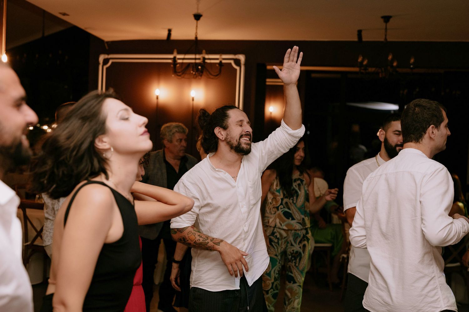 A group of people dancing and celebrating at a wedding reception with warm lighting and festive atmosphere.