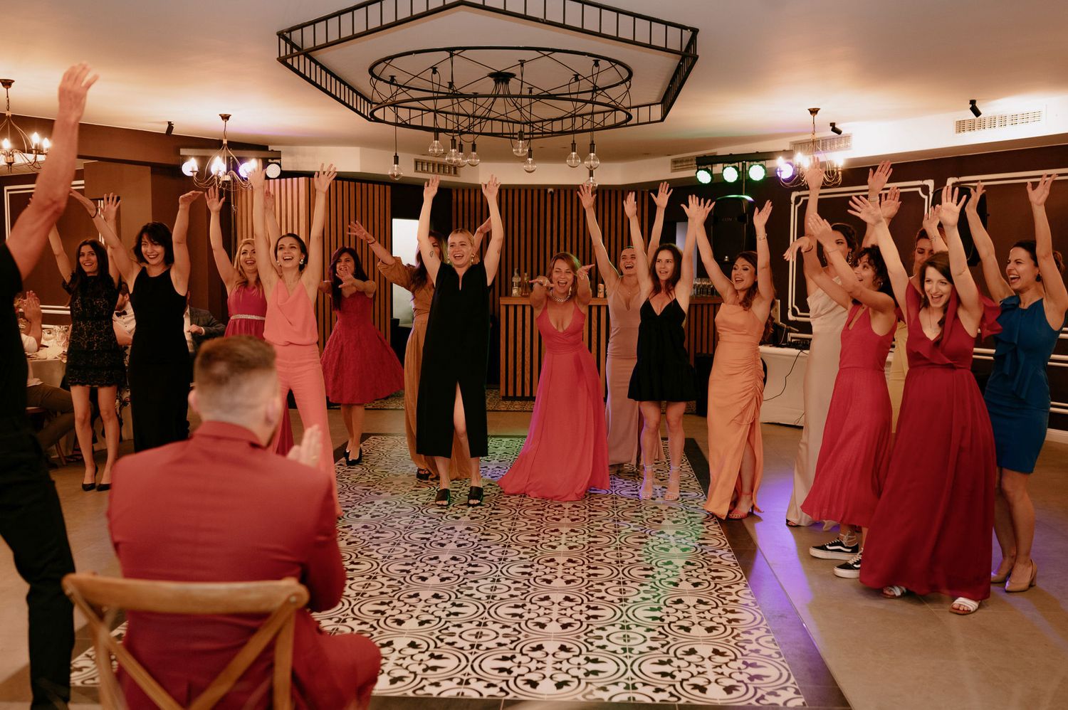 Wedding party dancing and celebrating on a dance floor with raised arms and red dresses in a reception venue.