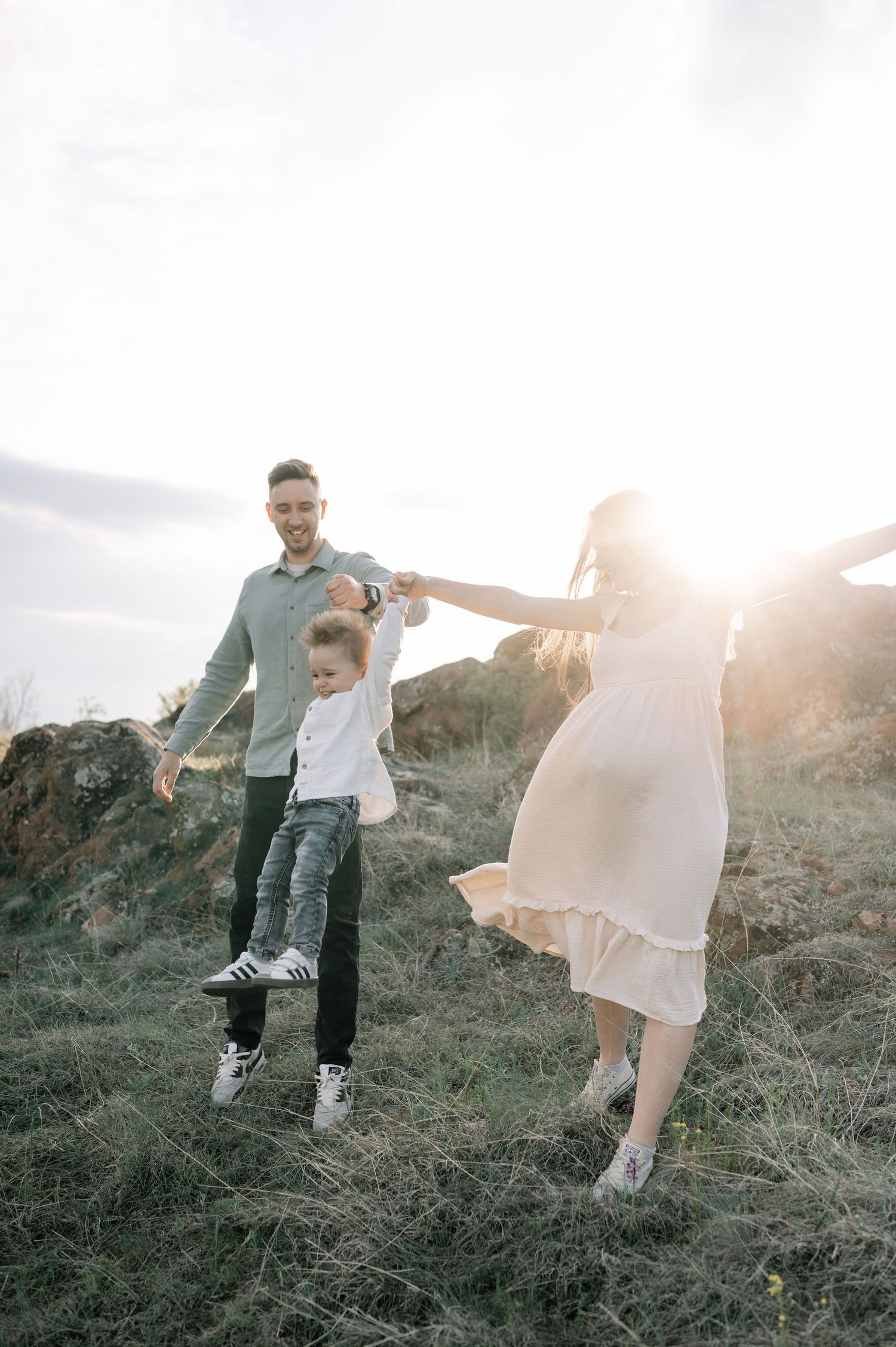 A family holds hands and dances together on a grassy hillside at sunset, creating a joyful silhouette against the sky.