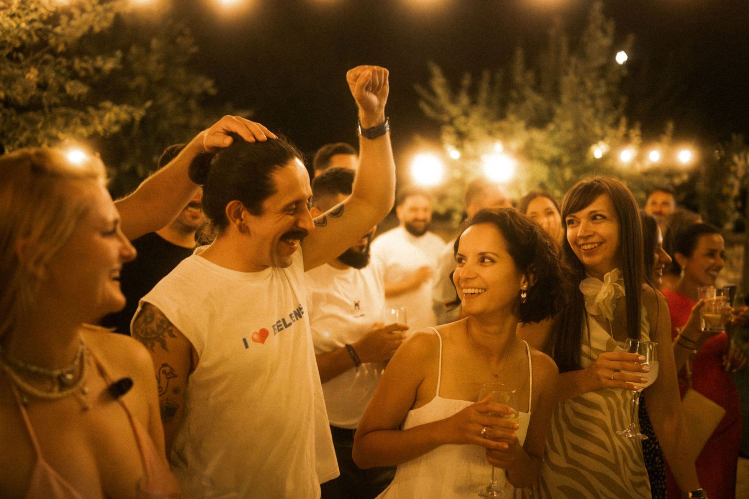 People dancing and celebrating at a romantic outdoor evening wedding reception under warm glowing lights.