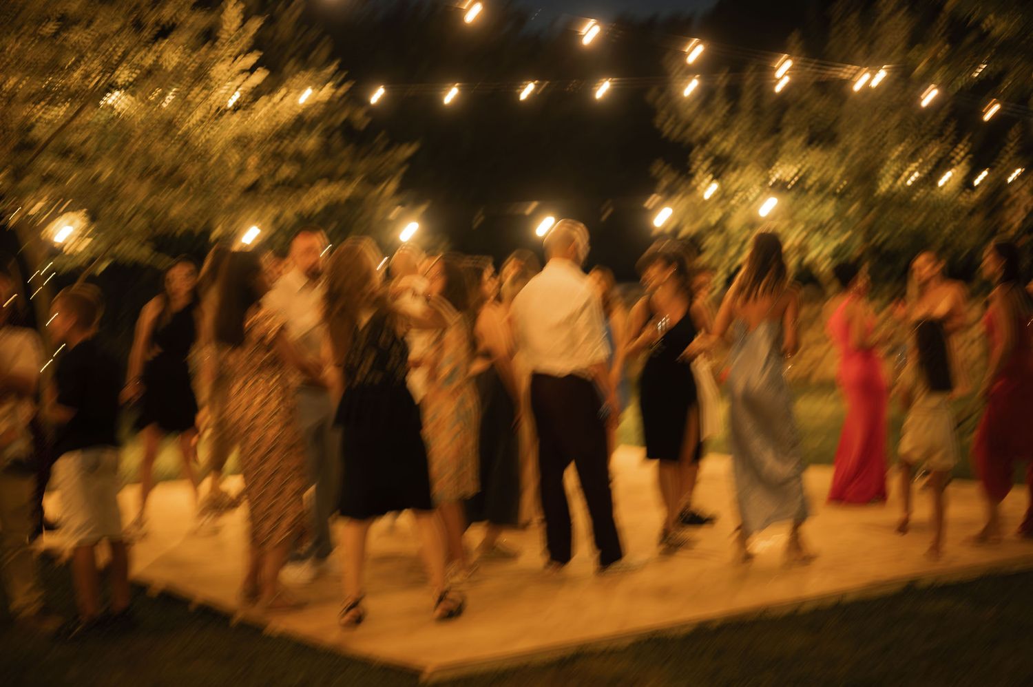 People dancing at an outdoor nighttime event with string lights illuminating the festive atmosphere.