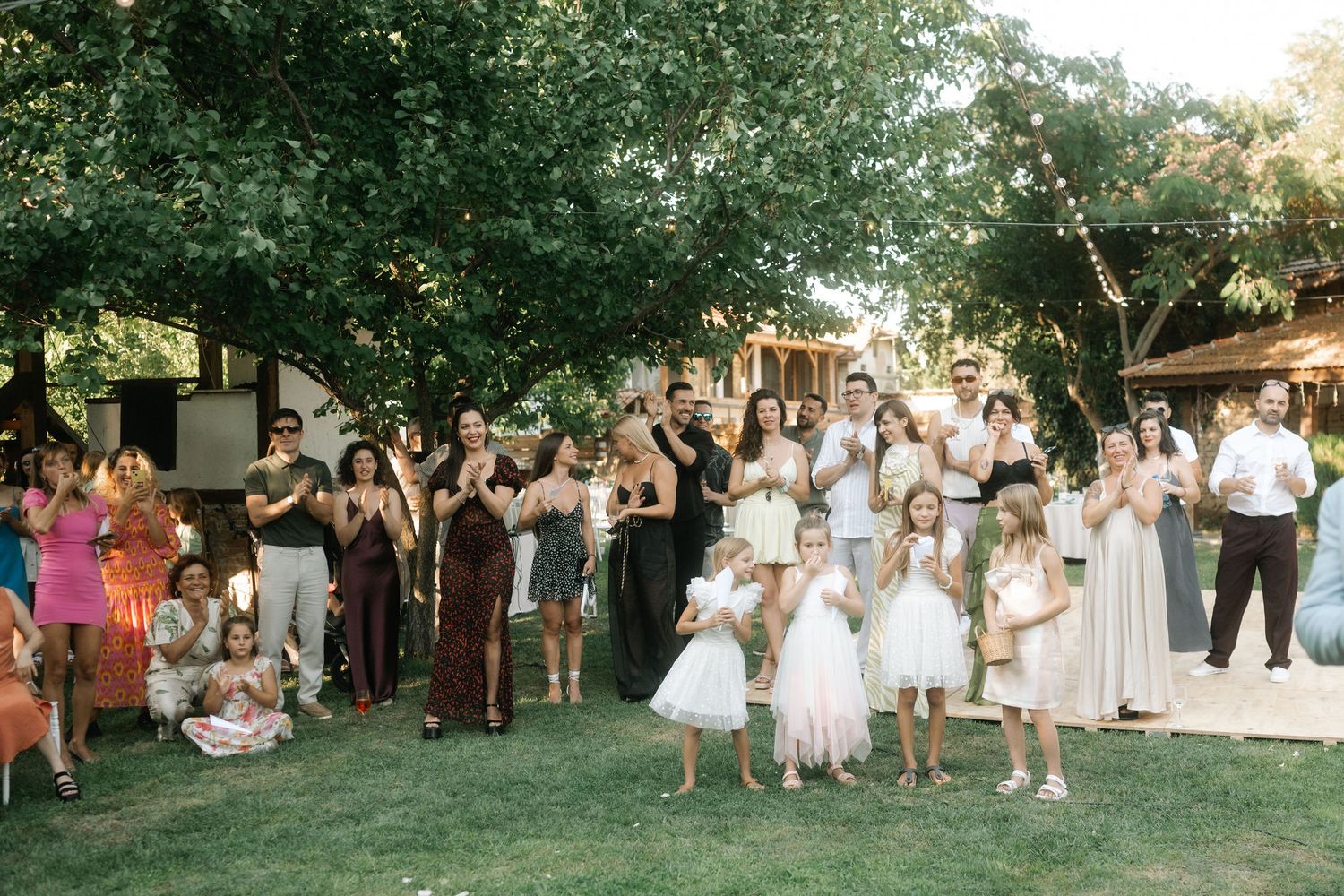 Wedding party dances together on a lawn during sunset at an outdoor summer celebration.