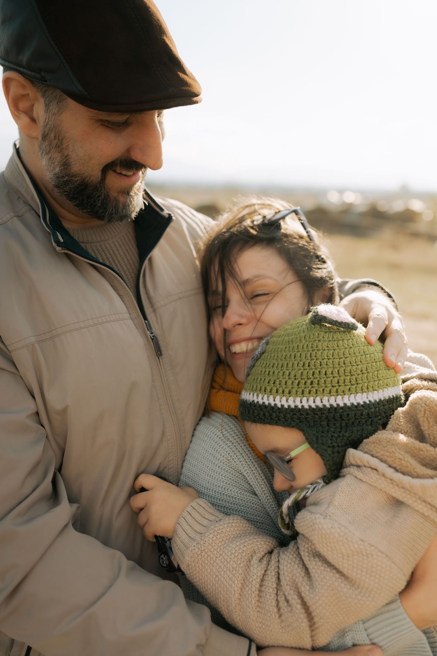 A couple shares an intimate embrace outdoors during golden hour, wearing casual winter attire.